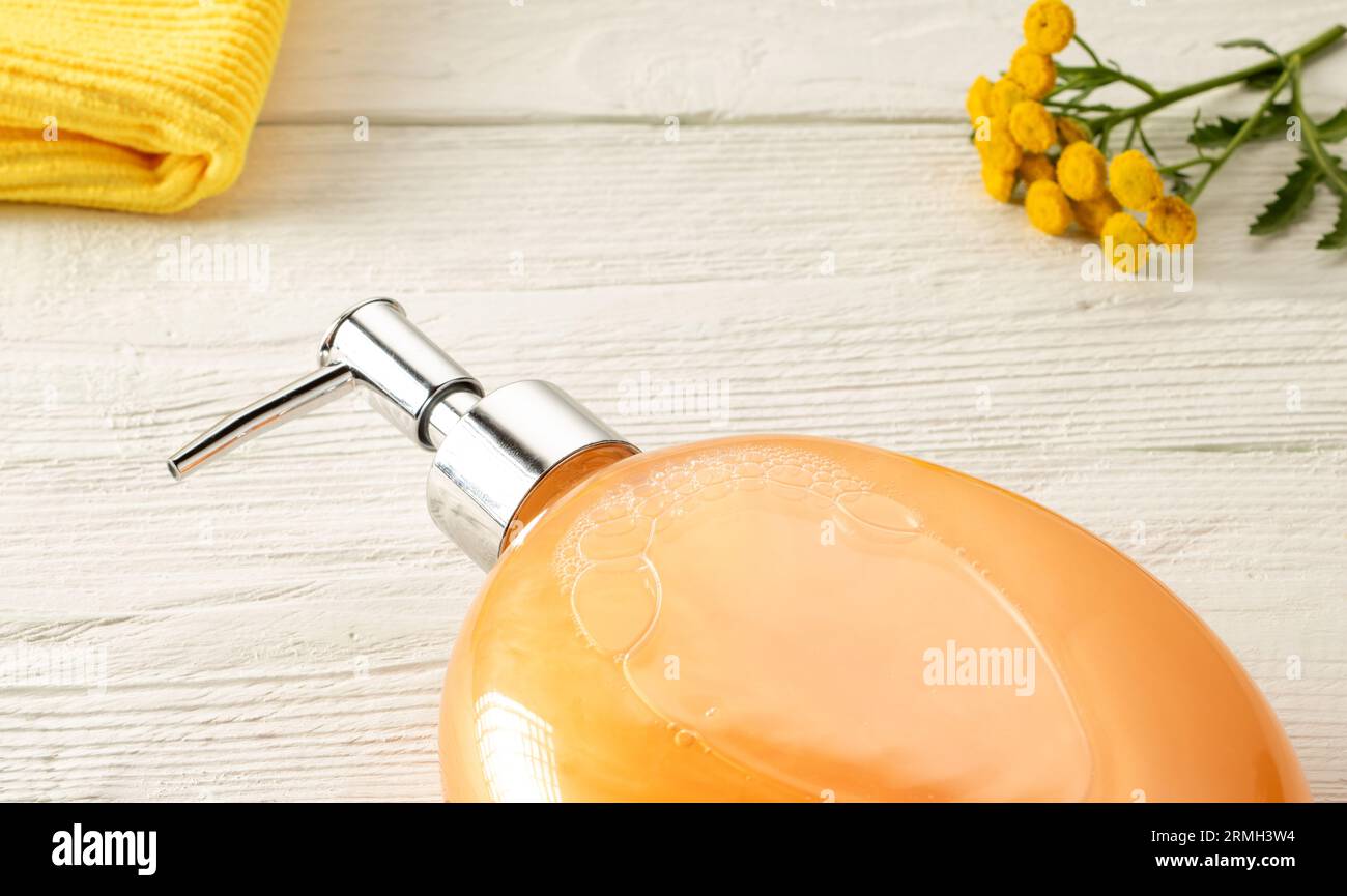 Badezimmeraccessoires in Orangetönen. Shampooflasche, Serviette und bunte tansy-Blume auf weißem Holztisch. Stockfoto