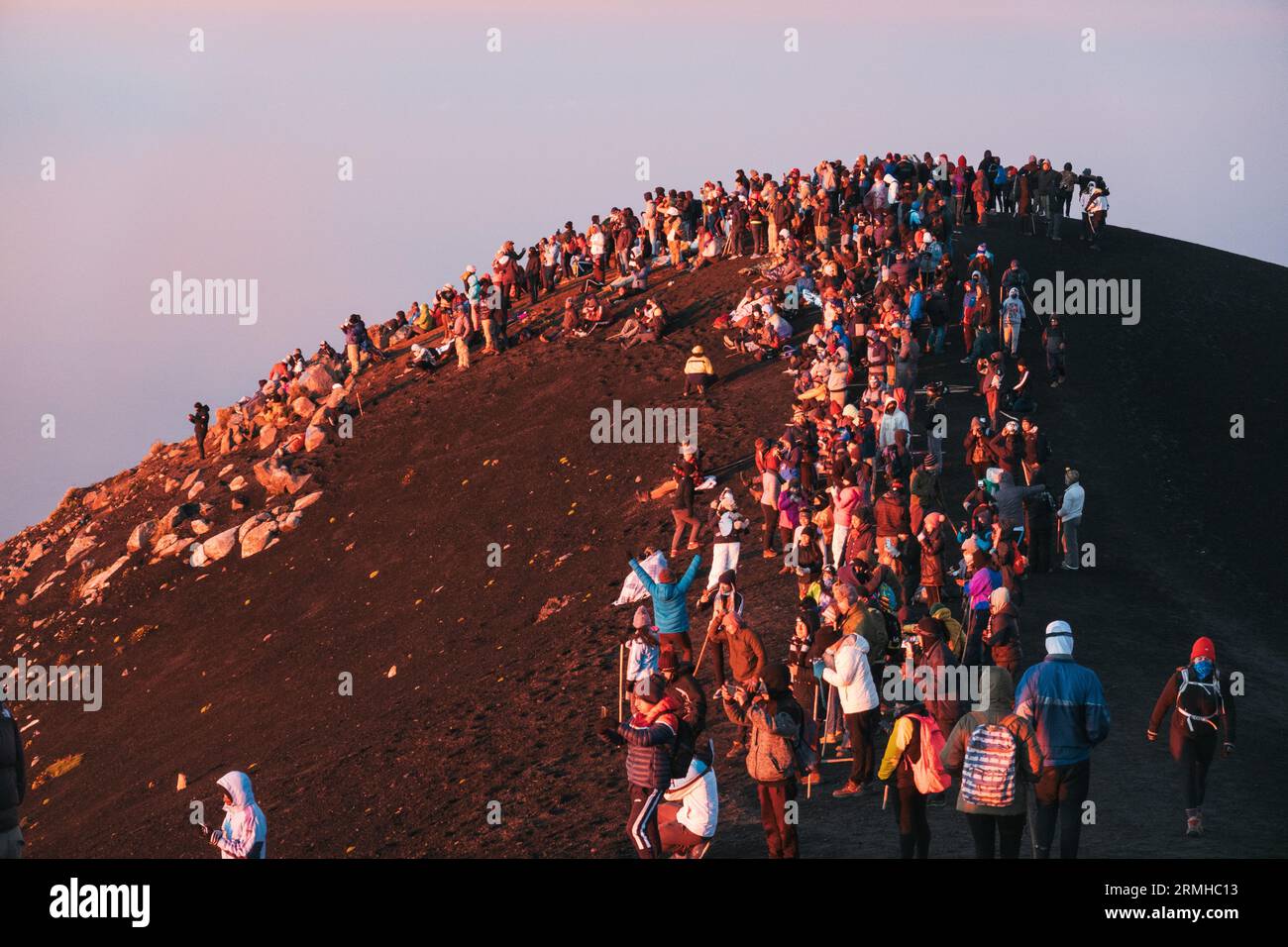Dutzende von Touristen drängen sich auf den Gipfel des ruhenden Acatenango-Vulkans in Guatemala, um den benachbarten und aktiven Fuego-Vulkan bei Sonnenaufgang zu beobachten Stockfoto