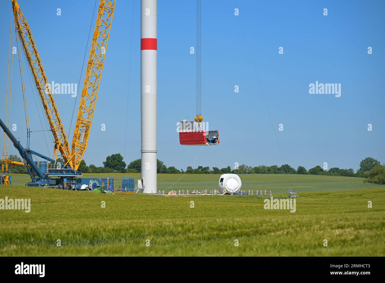 Baustelle einer Windkraftanlage, Kran, der das Maschinenhaus hebt, um es auf dem Turm zu installieren, Konzept für erneuerbare Energie und Energie, blauer Himmel, Kopierraum Stockfoto
