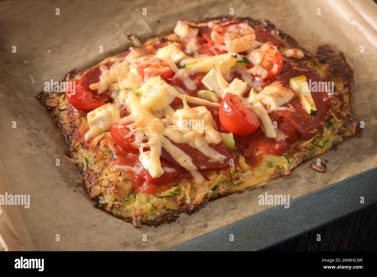 Ein Stück kohlenhydratarme Pizza auf einer Kruste aus Zucchini und Haferflocken, garniert mit Tomaten, Fetakäse und Salami auf einem Blech mit Backpapier, ausgewähltem Focu Stockfoto