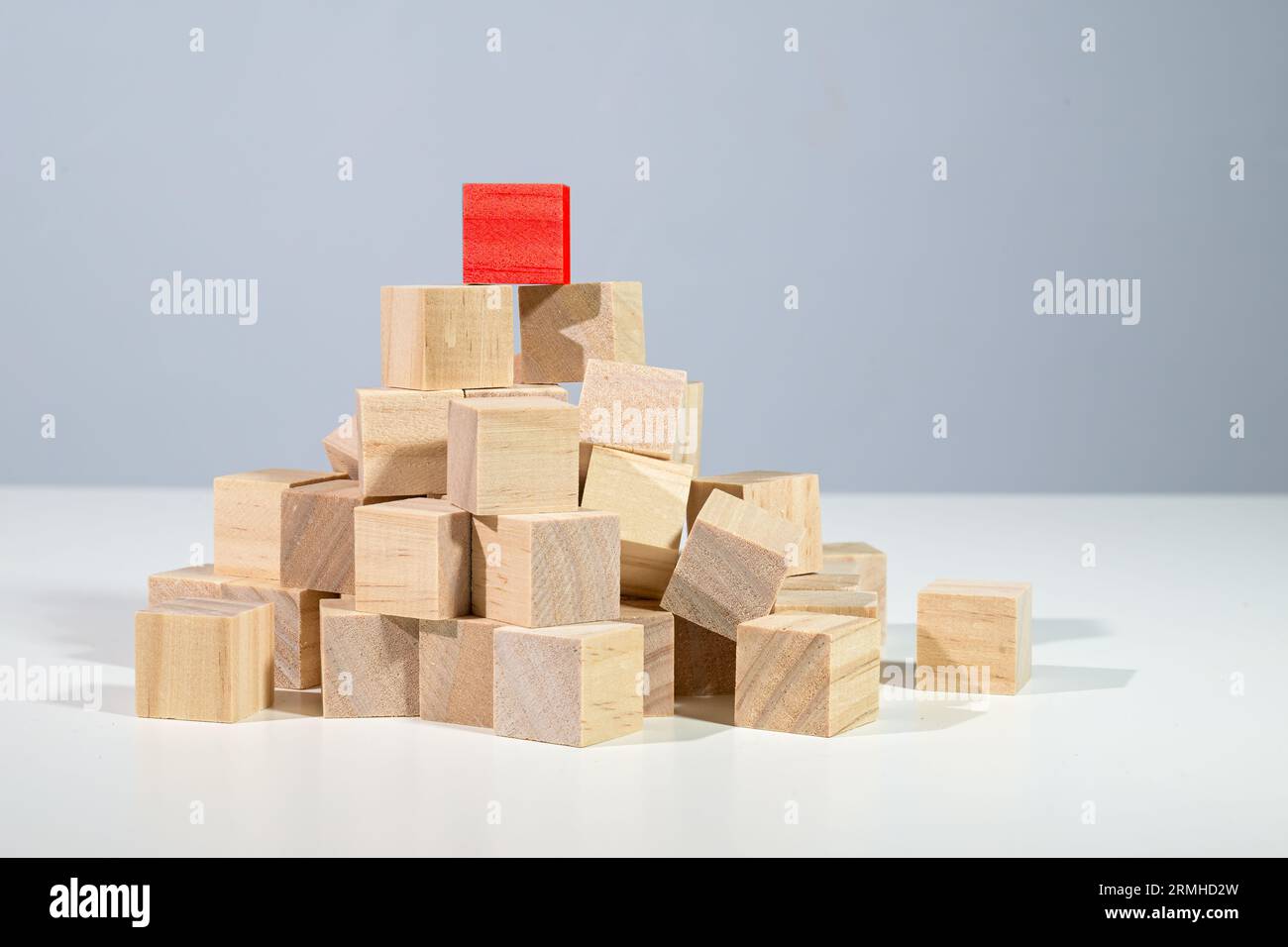 Roter Würfel, der auf einem Haufen aus hellen Holzwürfeln steht, Konzept für Geschäft, Karriere und Erfolg, grauer Hintergrund mit Kopierraum Stockfoto