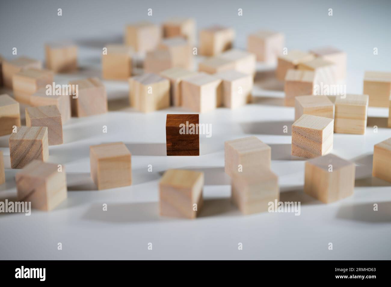 Einzelner Würfel aus dunklem Holz, der inmitten einer Menge heller Holzwürfel steht, soziales Konzept für Vielfalt, Andersartigkeit, Ausgrenzung und Integ Stockfoto