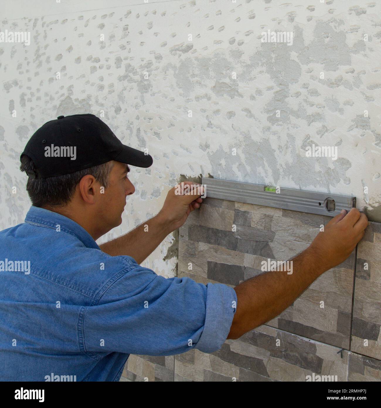Bild eines Kachels mit einer Ebene, um die Verlegung von Kacheln an einer Wand zu überprüfen. DIY-Renovierungsarbeiten. Stockfoto