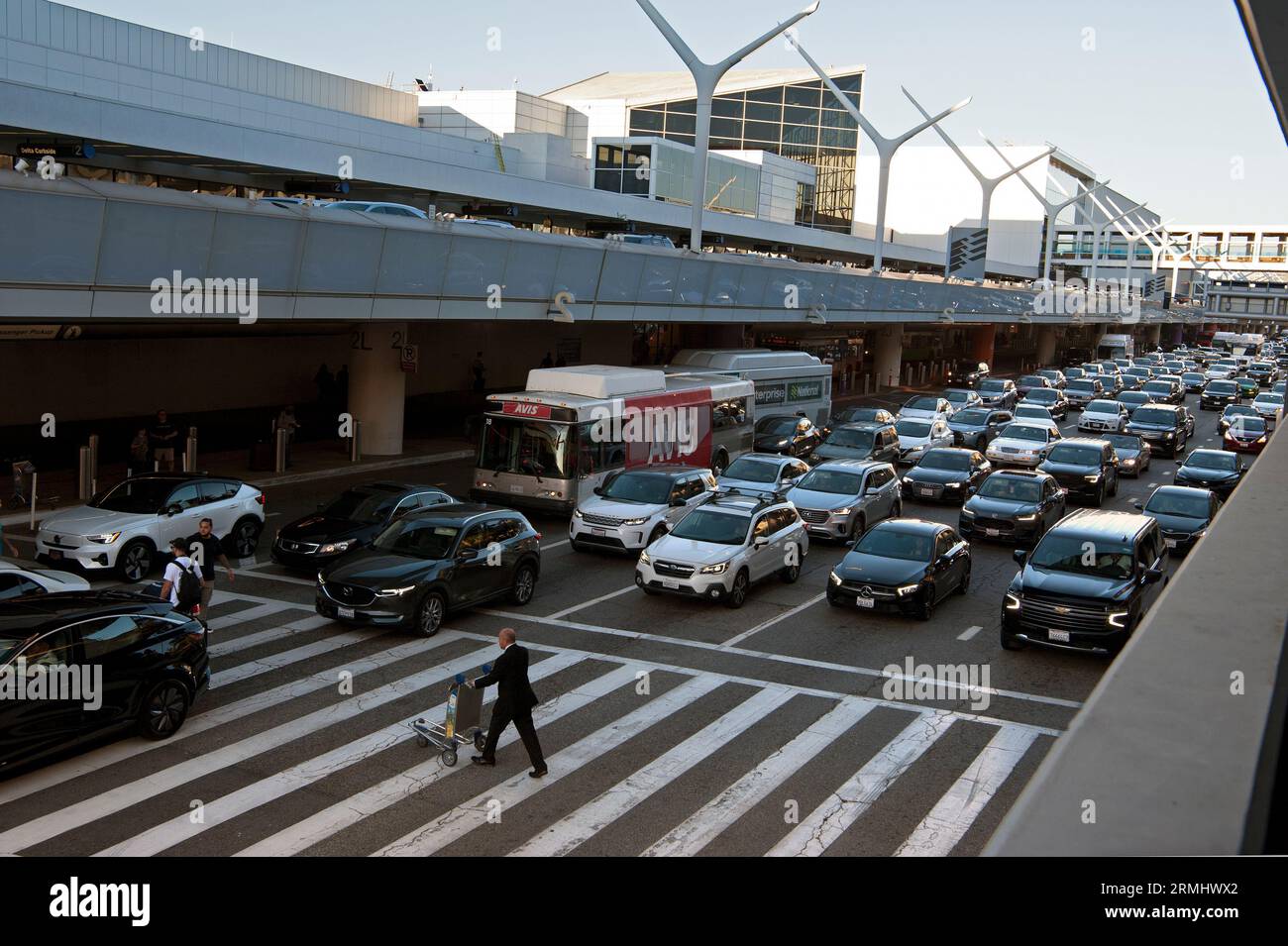 In Los Angeles, KALIFORNIEN, USA, hält der Verkehr im LAX für einen Mann mit Gepäckwagen an einem Crosswalk Stockfoto