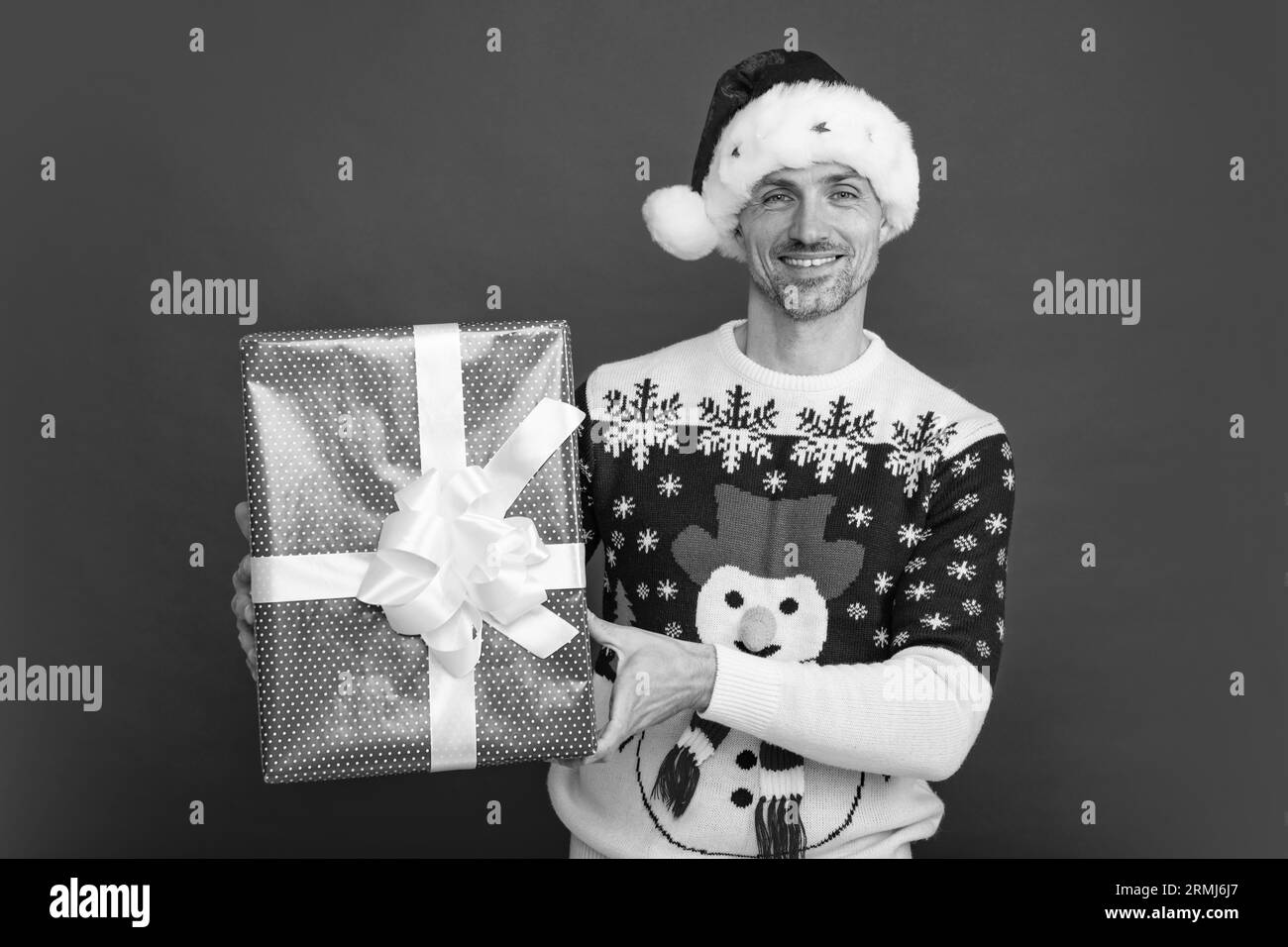 Porträt des Weihnachtsmanns im Pullover mit einer großen roten Geschenkbox isoliert auf rotem Hintergrund. Konzept der Weihnachtsfeiertage, Glück Stockfoto