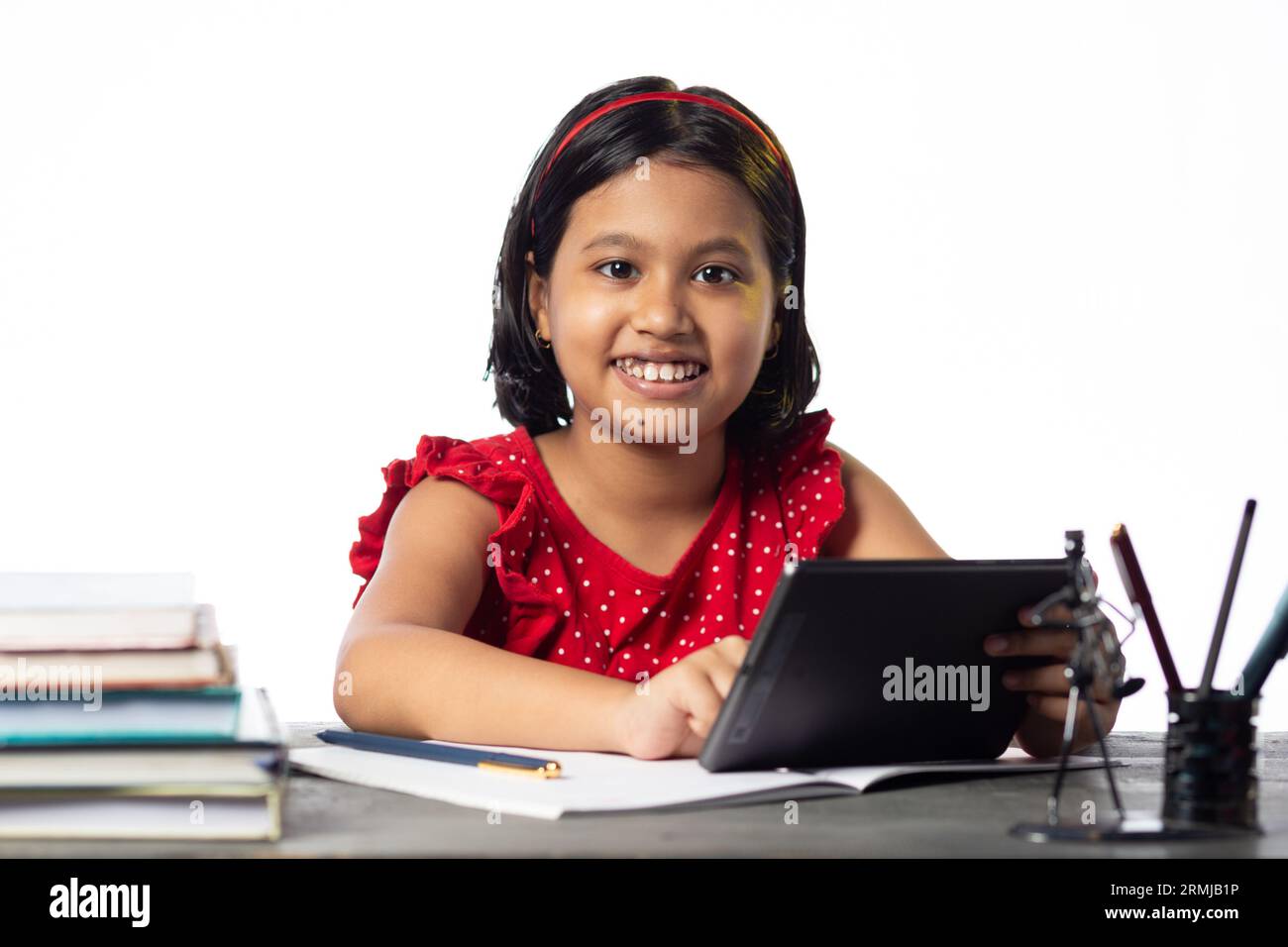 Ein hübsches indisches Mädchen, das mit einem Tablet am Tisch auf weißem Hintergrund lernt Stockfoto