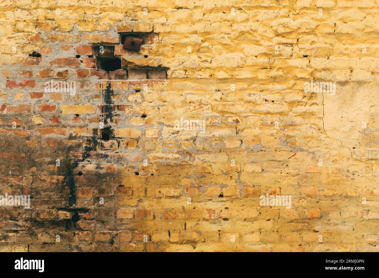 Alte gerissene und schmutzige gelbe Ziegelwand mit einzigartiger abgenutzter Textur und Muster der Oberfläche als abstrakter Hintergrund für Design Stockfoto
