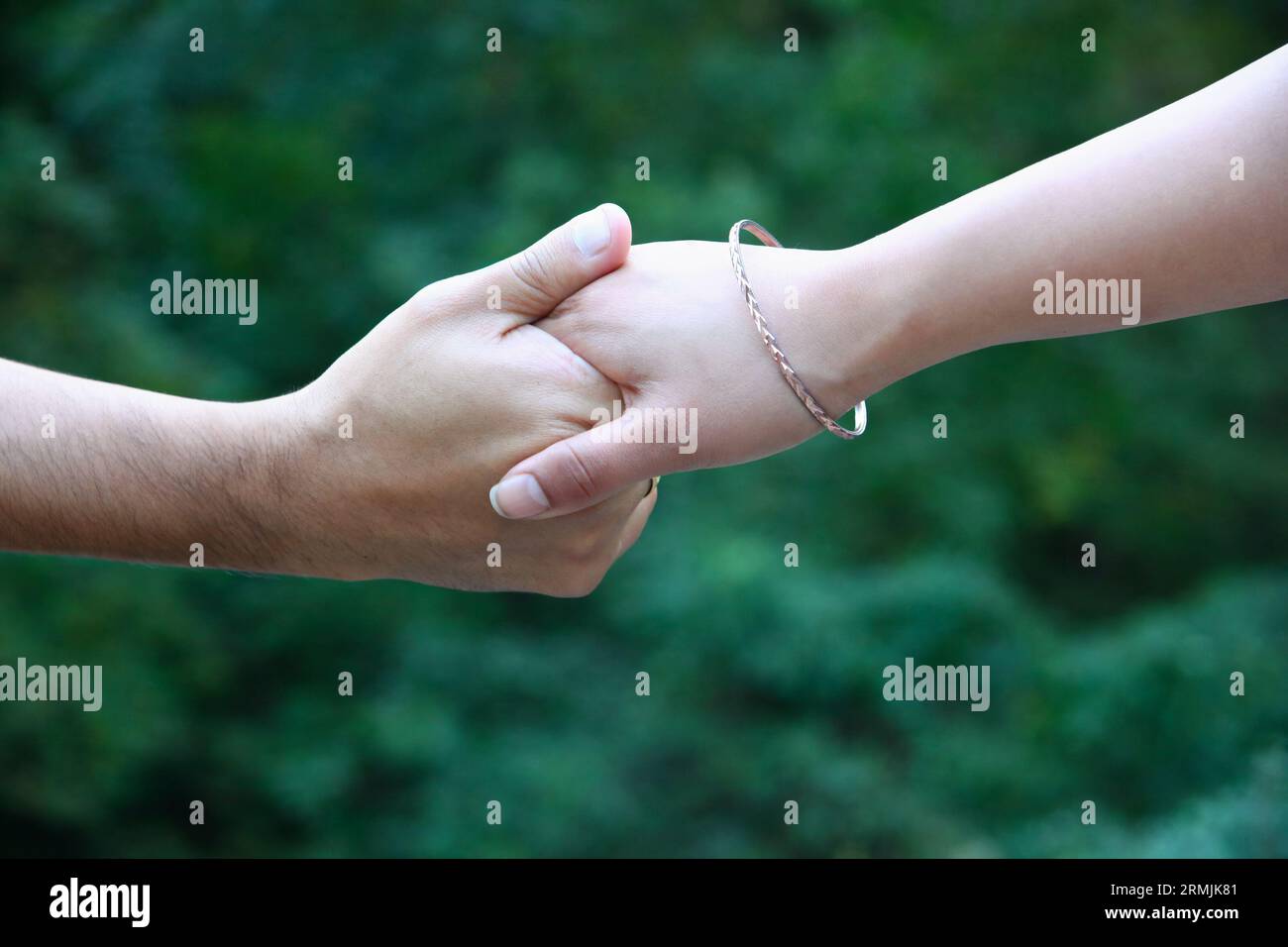 Nahaufnahme der Hände eines Mannes und einer Frau, die sich gegenseitig halten. Die Frau trägt ein Armband. Hintergrund ist tiefgrün. Stockfoto