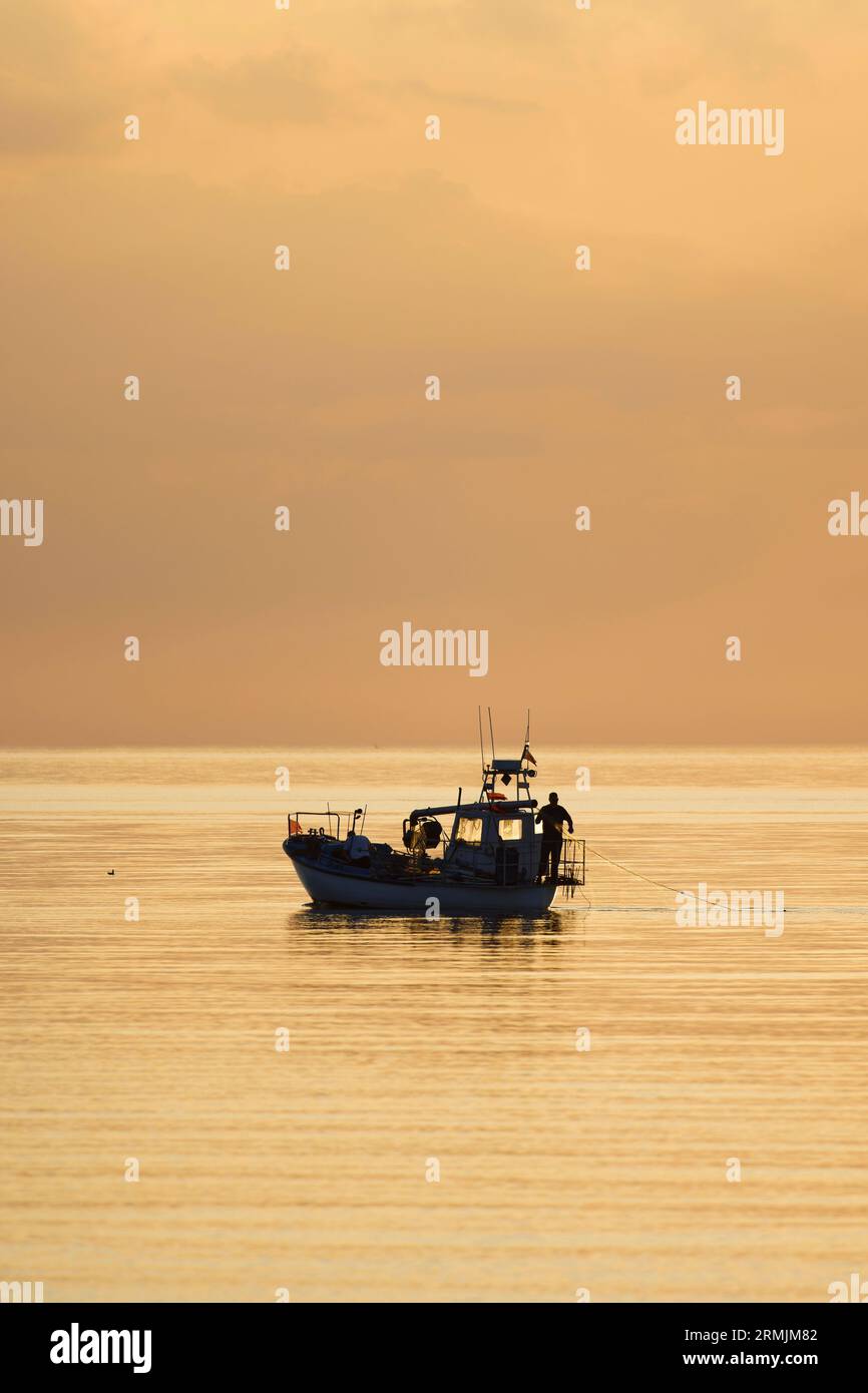 Kleines kommerzielles Fischerboot, das bei Sonnenuntergang zum ruhigen Meer fährt Stockfoto