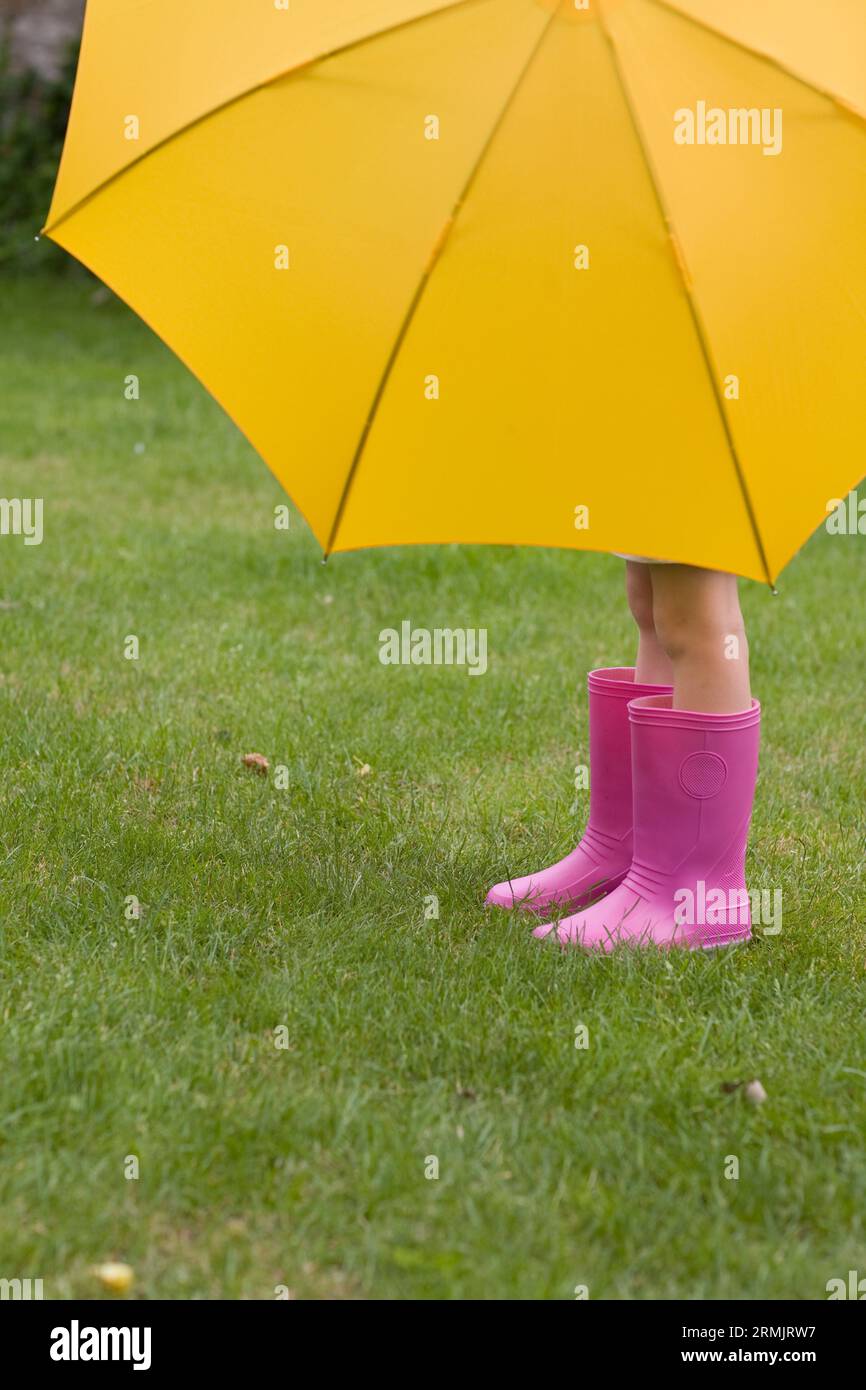 Junges Mädchen in rosa Stiefel unter gelben Regenschirm Stockfoto