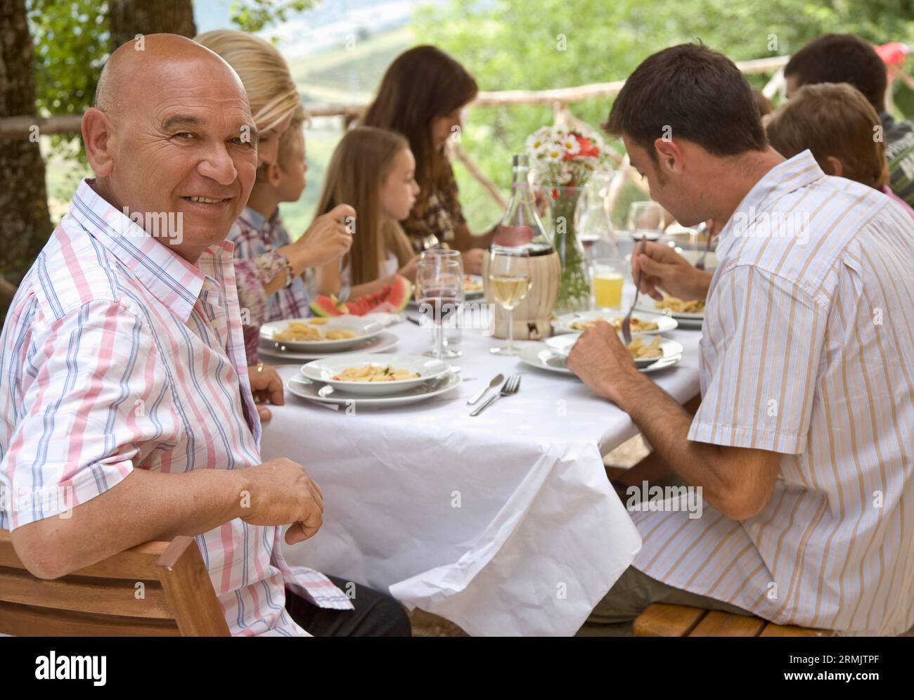 Eine große Familie sitzt am Tisch und serviert Pasta mit Großvater im Vordergrund Stockfoto