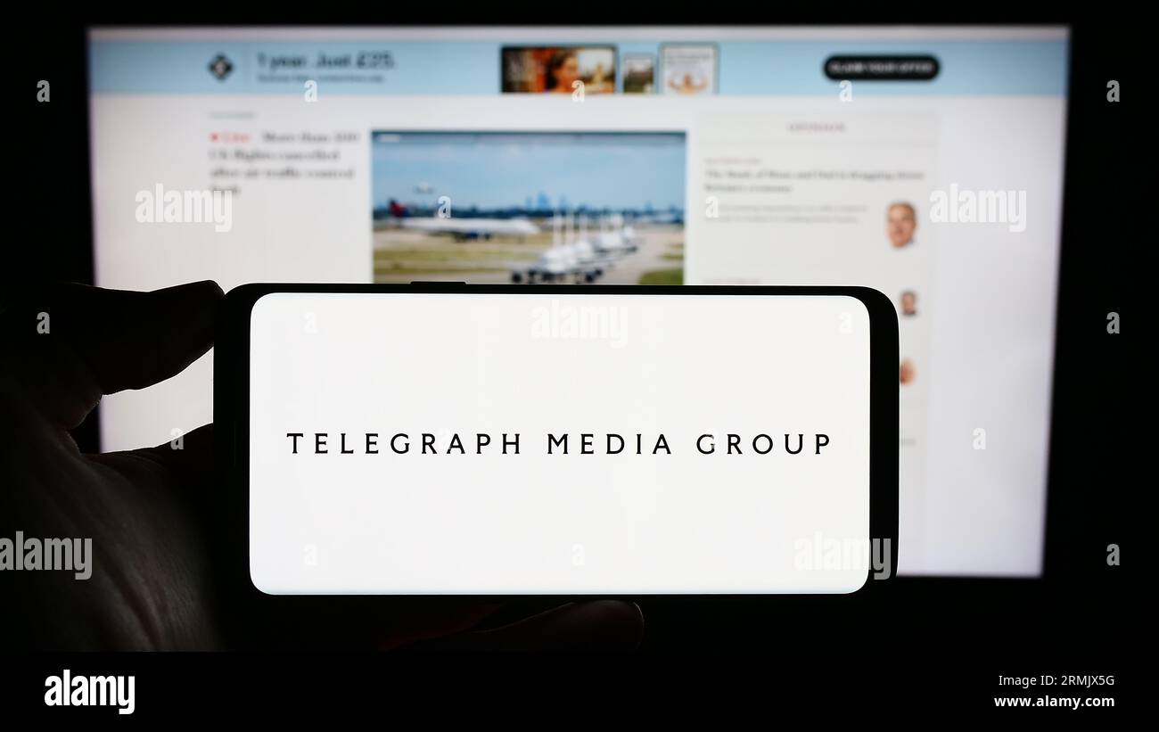 Person, die ein Mobiltelefon mit dem Logo der Firma Telegraph Media Group Limited (TMG) auf dem Bildschirm vor der Webseite hält. Konzentrieren Sie sich auf das Display des Telefons. Stockfoto