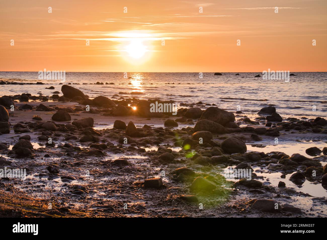 Sonnenuntergang, Steinstrand mit kleinen und großen Felsen vor dem beleuchteten Meer. Lichtwellen. Poelinsel an der Ostsee. Naturfoto von den coas Stockfoto