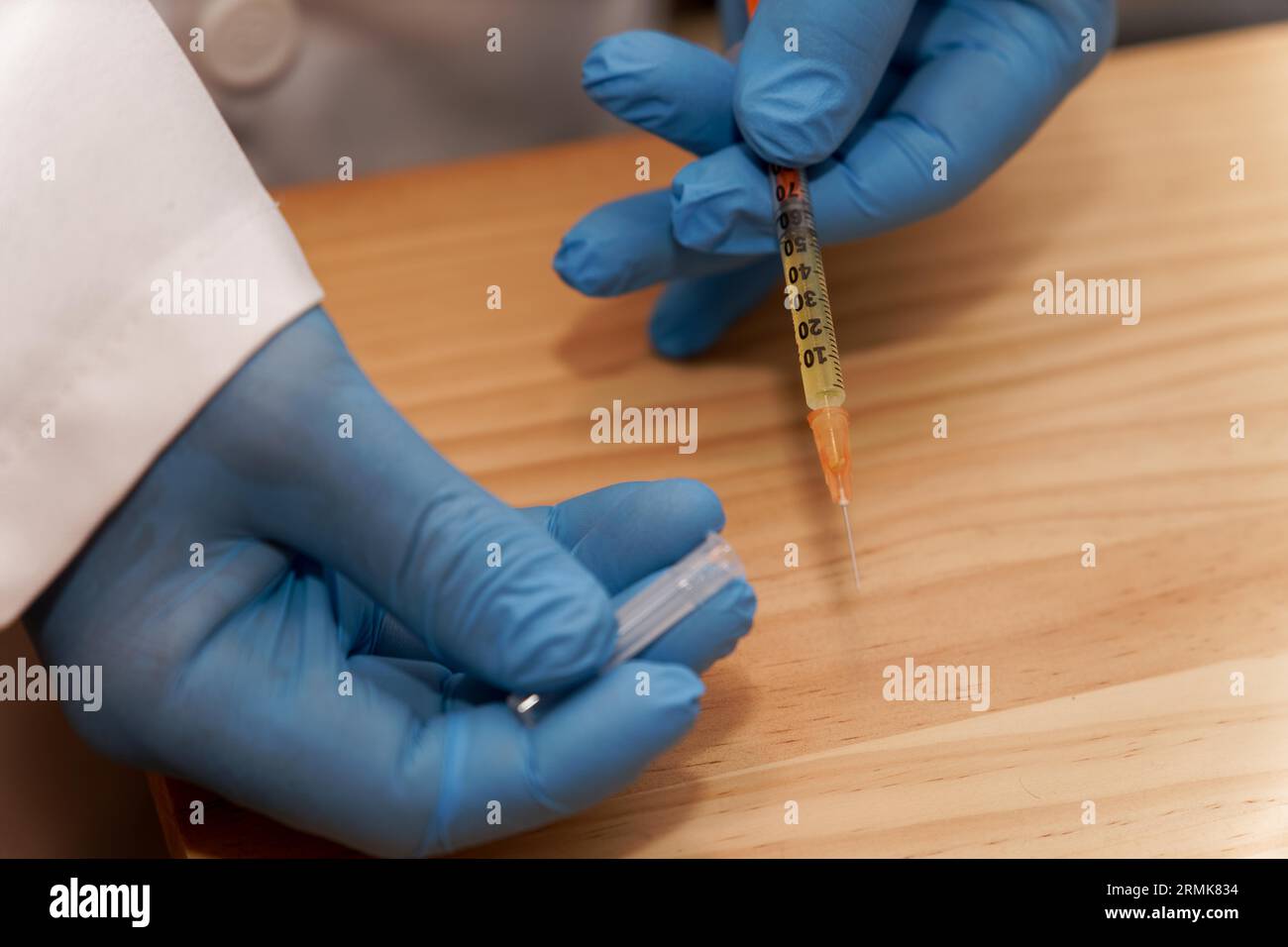 Arzthandschuhe in blauen Latexhandschuhen mit einer Spritze in der Hand auf dem Tisch in seiner Praxis Stockfoto