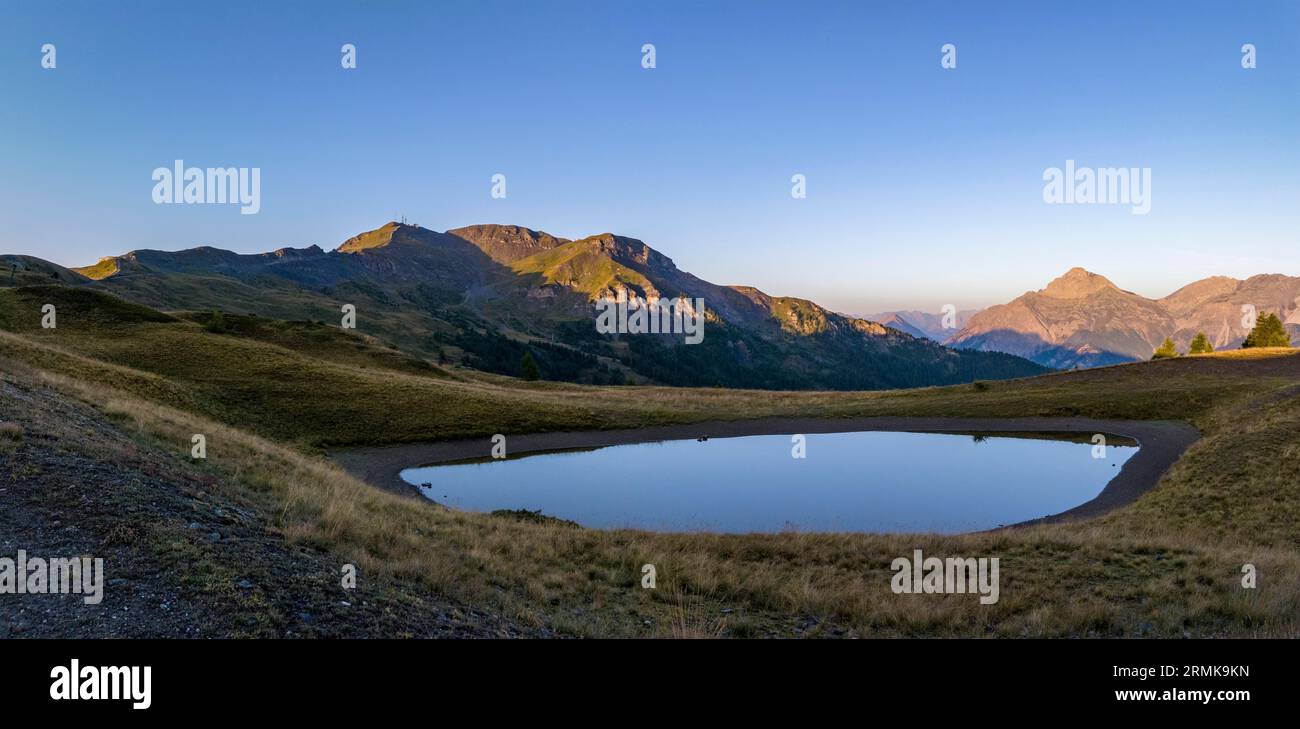 Mogenstimmung, Bergsee und Assietta-Bergstraße bei Colle Basset, im Hintergrund die Alpen im italienisch-französischen Grenzgebiet, Sauze d’Oulx Stockfoto