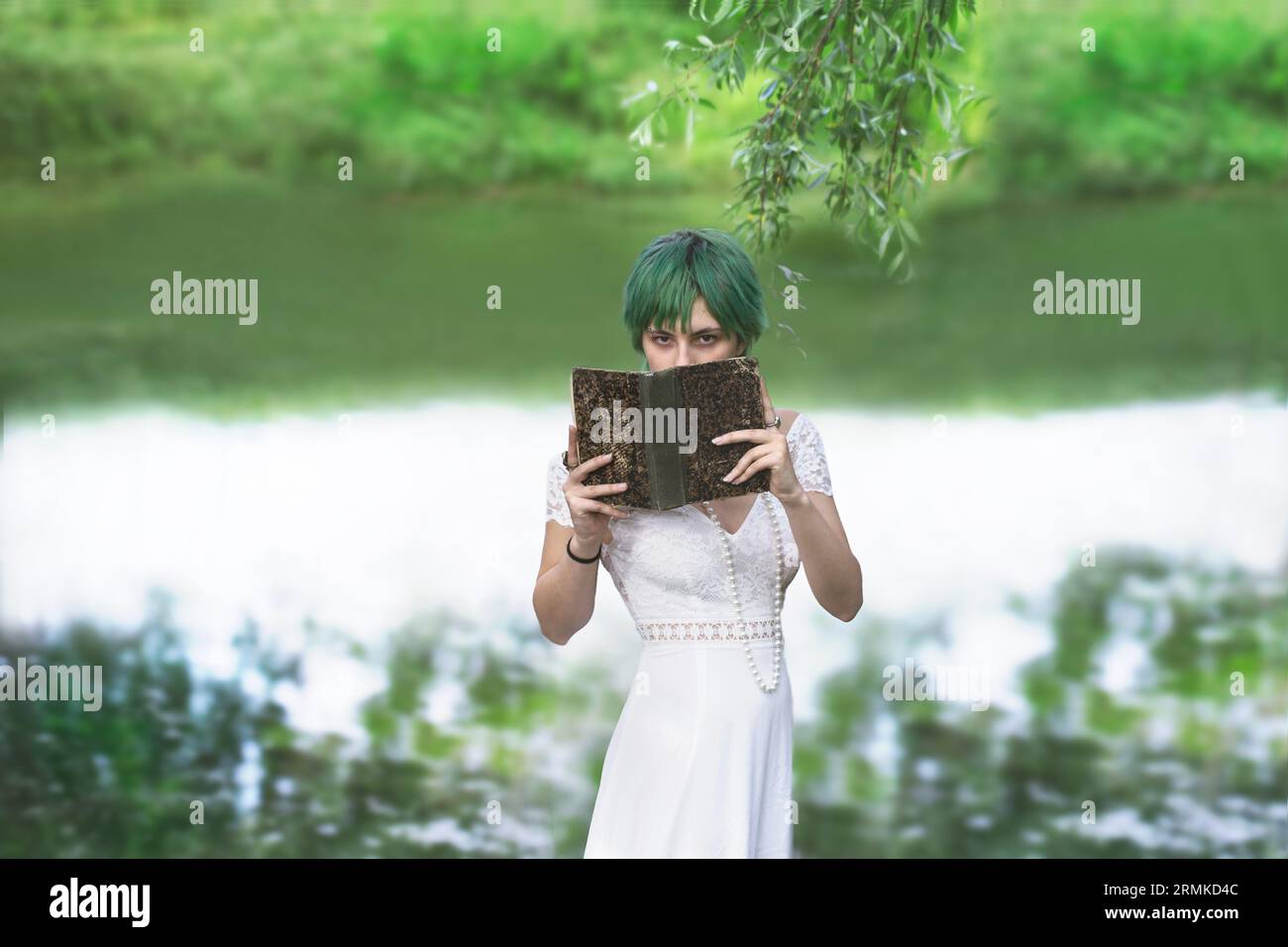 Mysteriöses Mädchen, das ihr Gesicht zeigt, versteckt durch ein Buch inmitten der Natur Stockfoto