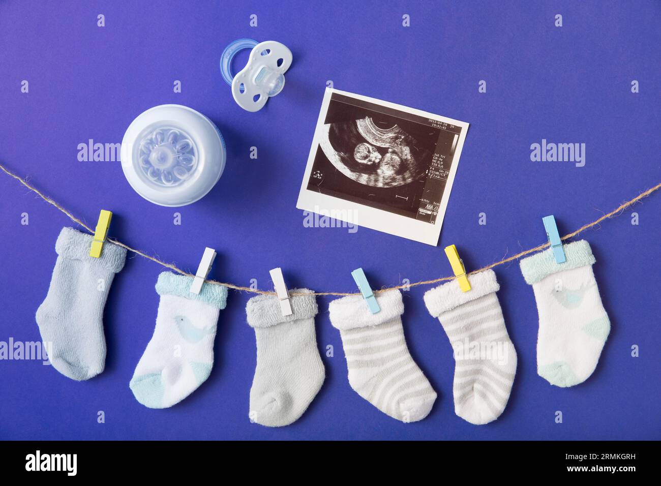 Babysocken hängende Kleidung mit Milchflaschenschnuller, blauem Ultraschallbild vor blauem Hintergrund Stockfoto