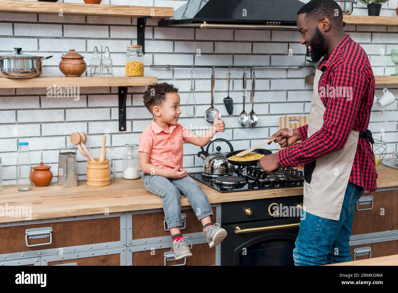 Der schwarze Vater kocht Essen, während der Sohn den Daumen zeigt Stockfoto