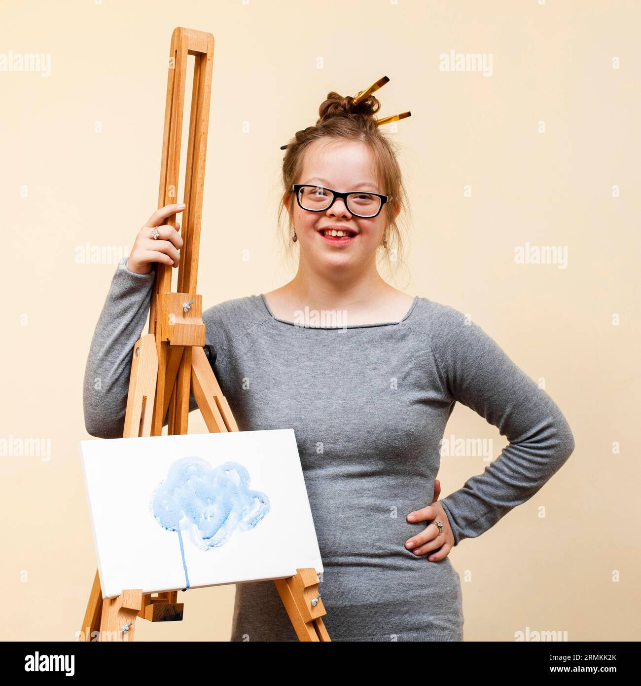 Smiley-Mädchen mit Down-Syndrom, das mit Staffelei posiert Stockfoto