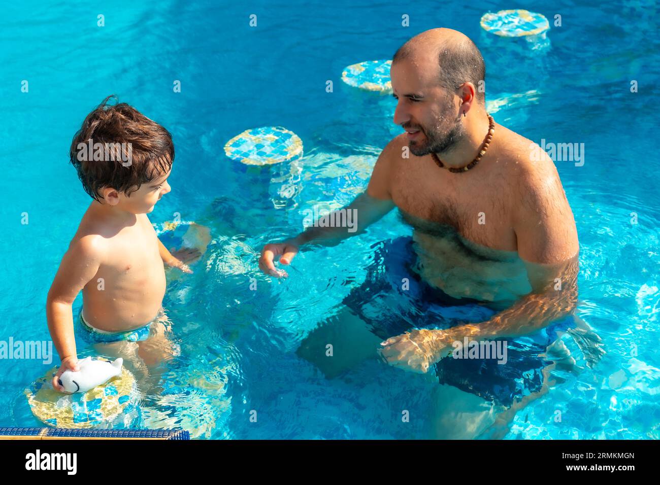 Vater und Sohn sind im Sommer im Pool, spielen und lächeln im Urlaub Stockfoto