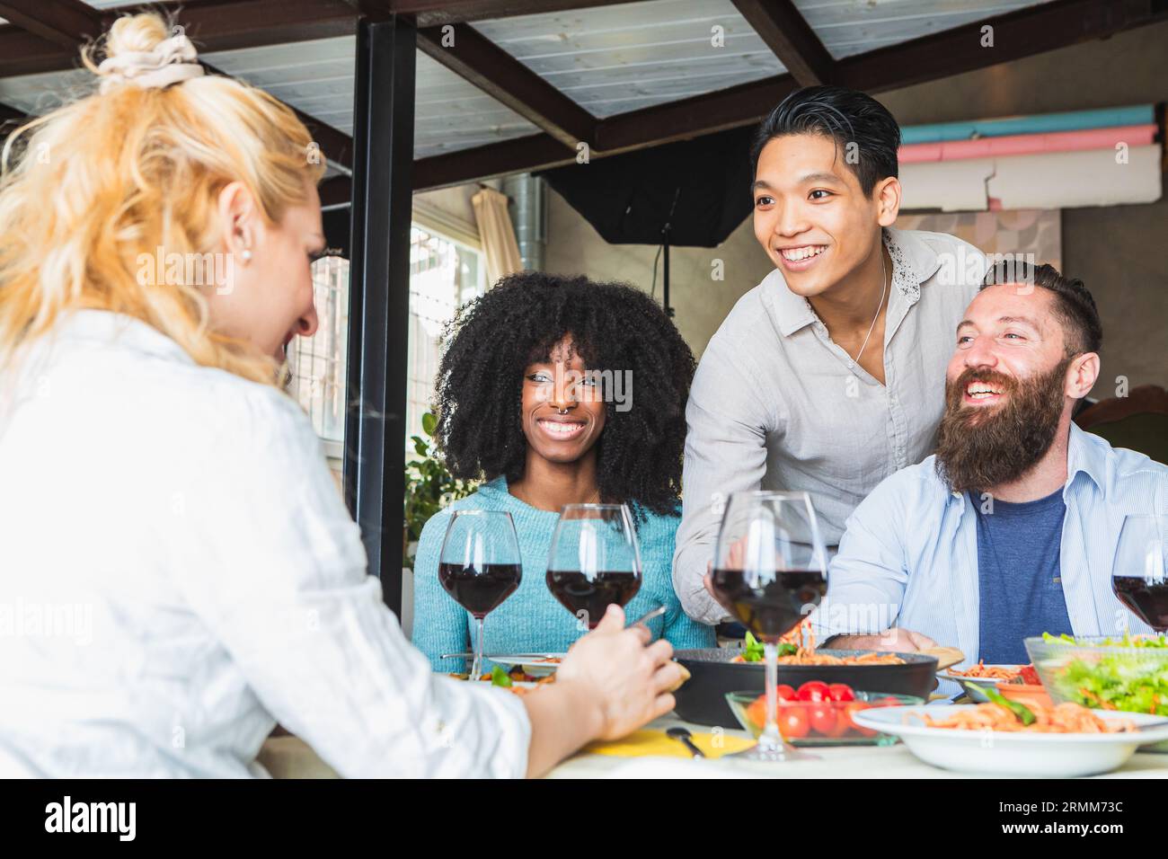 Viele Menschen trinken Rotwein in der Mittagspause. Glückliche Freunde, die zu Hause Pasta-Dinner feiern. Essen- und Getränkekonzept mit Jungs und Mädels di Stockfoto