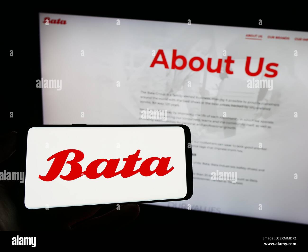 Person, die ein Mobiltelefon mit dem Logo des Schuhherstellers Bata Corporation auf dem Bildschirm vor der geschäftlichen Webseite hält. Konzentrieren Sie sich auf das Display des Telefons. Stockfoto