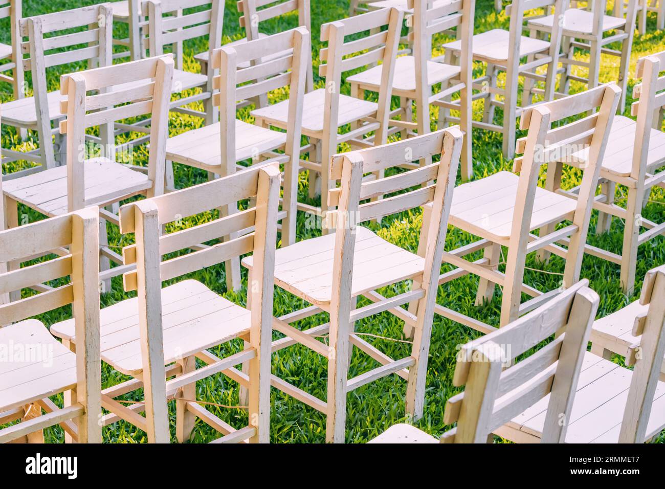 Die Hochzeitsszene der Natur: Eine wunderschön eingerichtete Gartenhochzeit mit weißen Stühlen vor der grünen Kulisse fängt das Wesen eines eleganten Außenbereichs ein Stockfoto