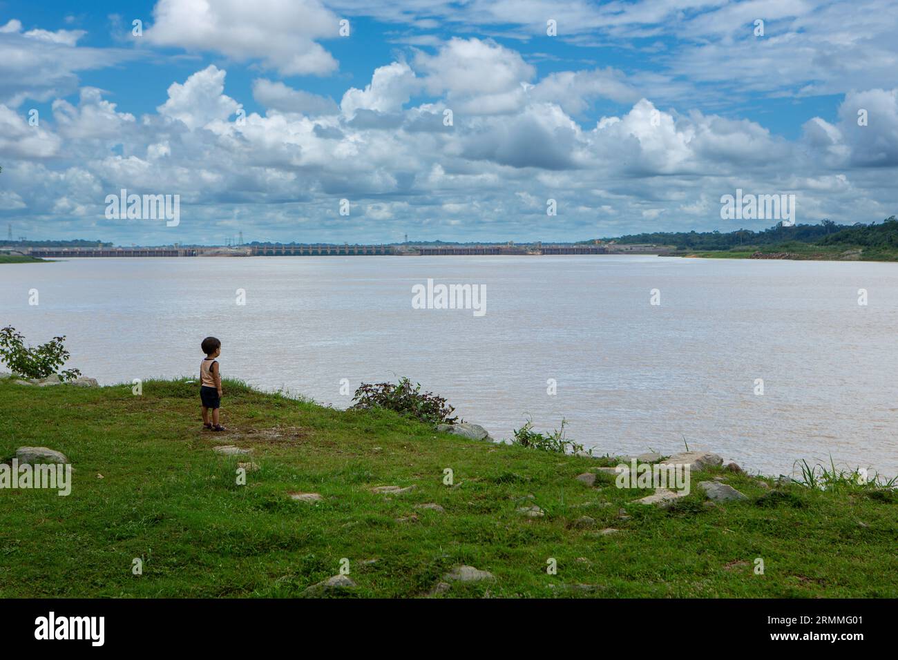 Einsamer, nicht identifizierter Junge am Ufer des Flusses Madeira und Santo Antonio Wasserkraftwerk im Hintergrund in Amazon, Rondonia, Brasilien. Stockfoto