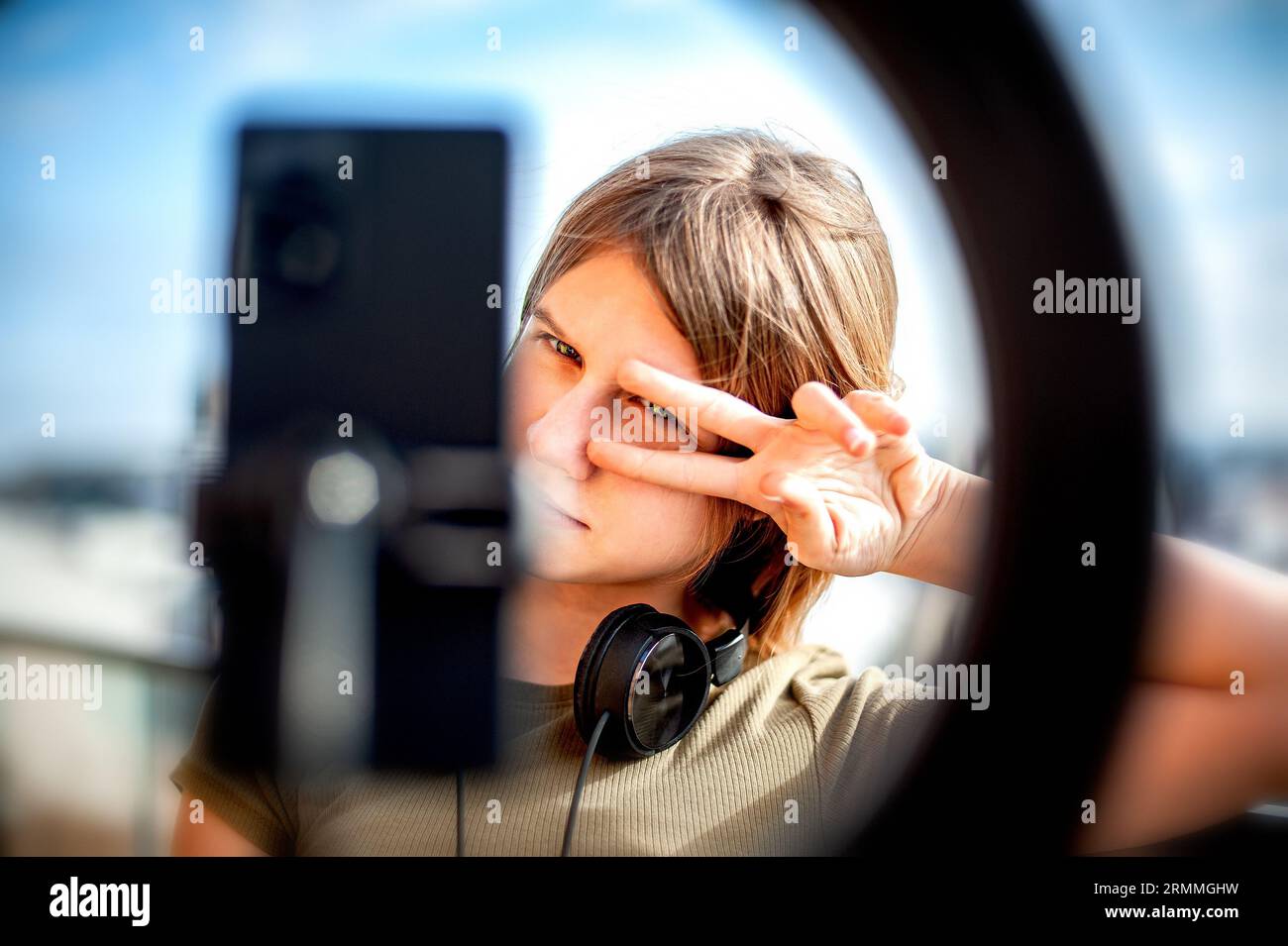 Teenager-Mädchen Social Media Blogger, die Video aufzeichnen und auf dem Balkon des Gebäudes ein Smartphone auf einem Stativ mit Ringlicht betrachten. Stockfoto
