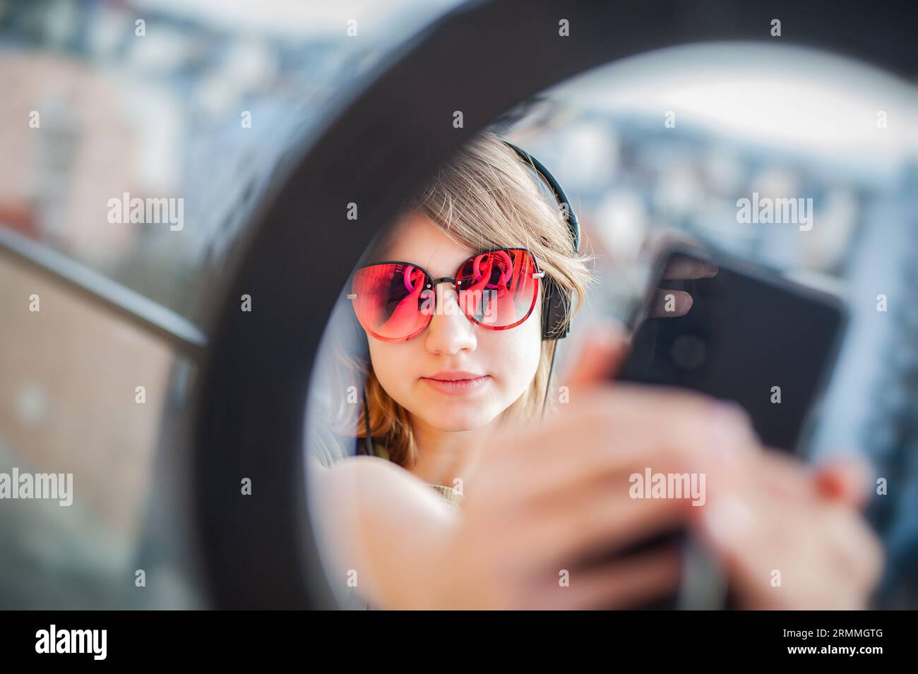 Teenager-Mädchen Social Media Blogger, die Video aufzeichnen und auf dem Balkon des Gebäudes ein Smartphone auf einem Stativ mit Ringlicht betrachten. Stockfoto