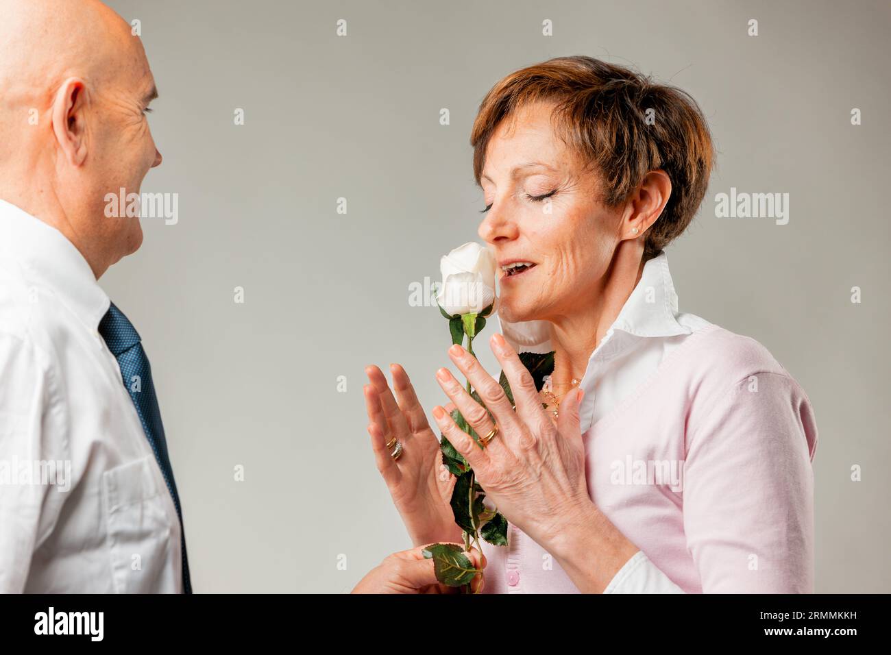 Diese weiße Rose riecht köstlich, der Duft unserer Liebe, mein Schatz. Wir haben uns schon so lange geliebt, und doch scheint es wie gestern. Älterer Mann Stockfoto