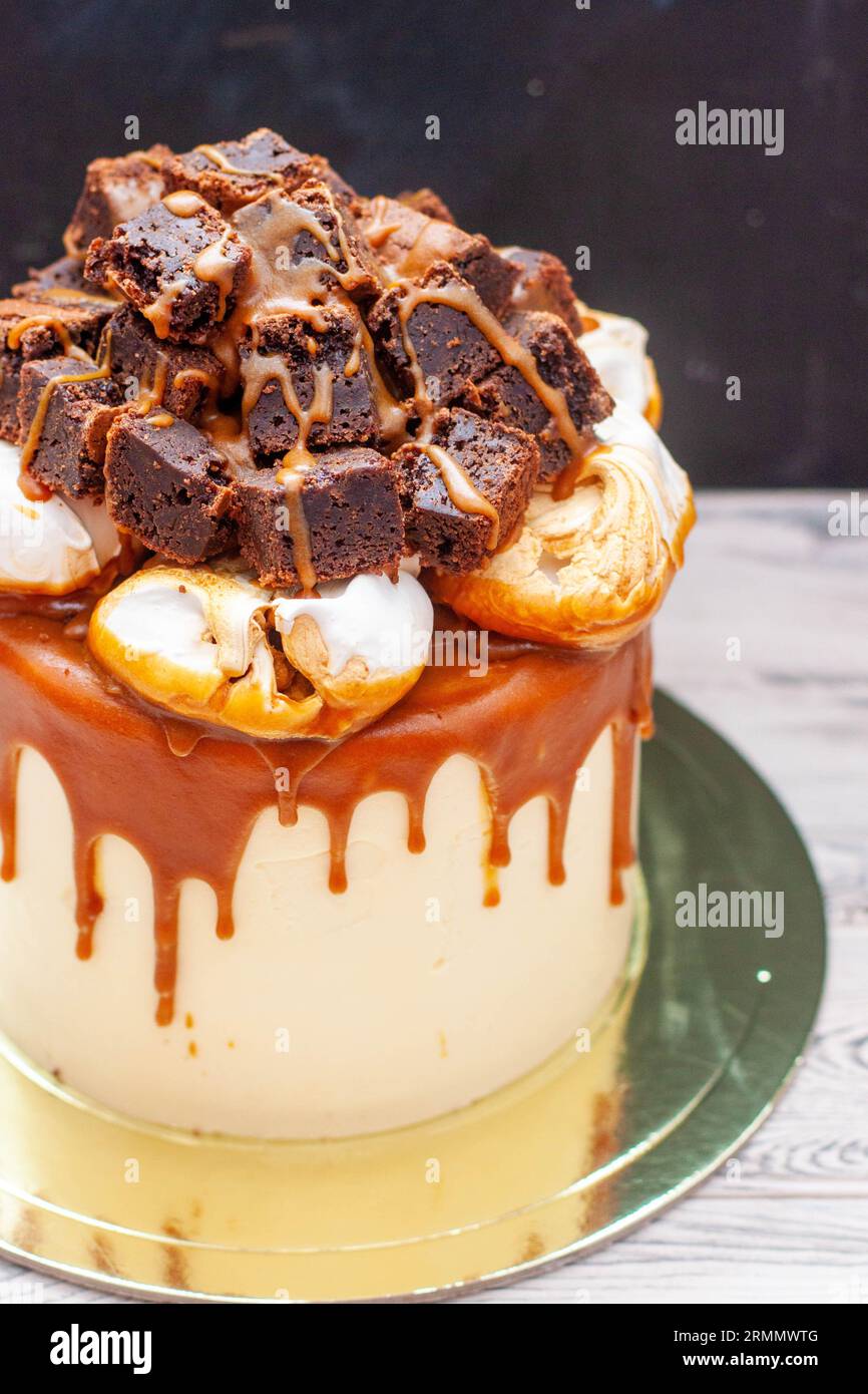 Köstlicher Vanillekuchen mit geschnittenen Brownie-Stücken, Meringue-Wolken und geschmolzener gesalzener Karamellsauce Stockfoto