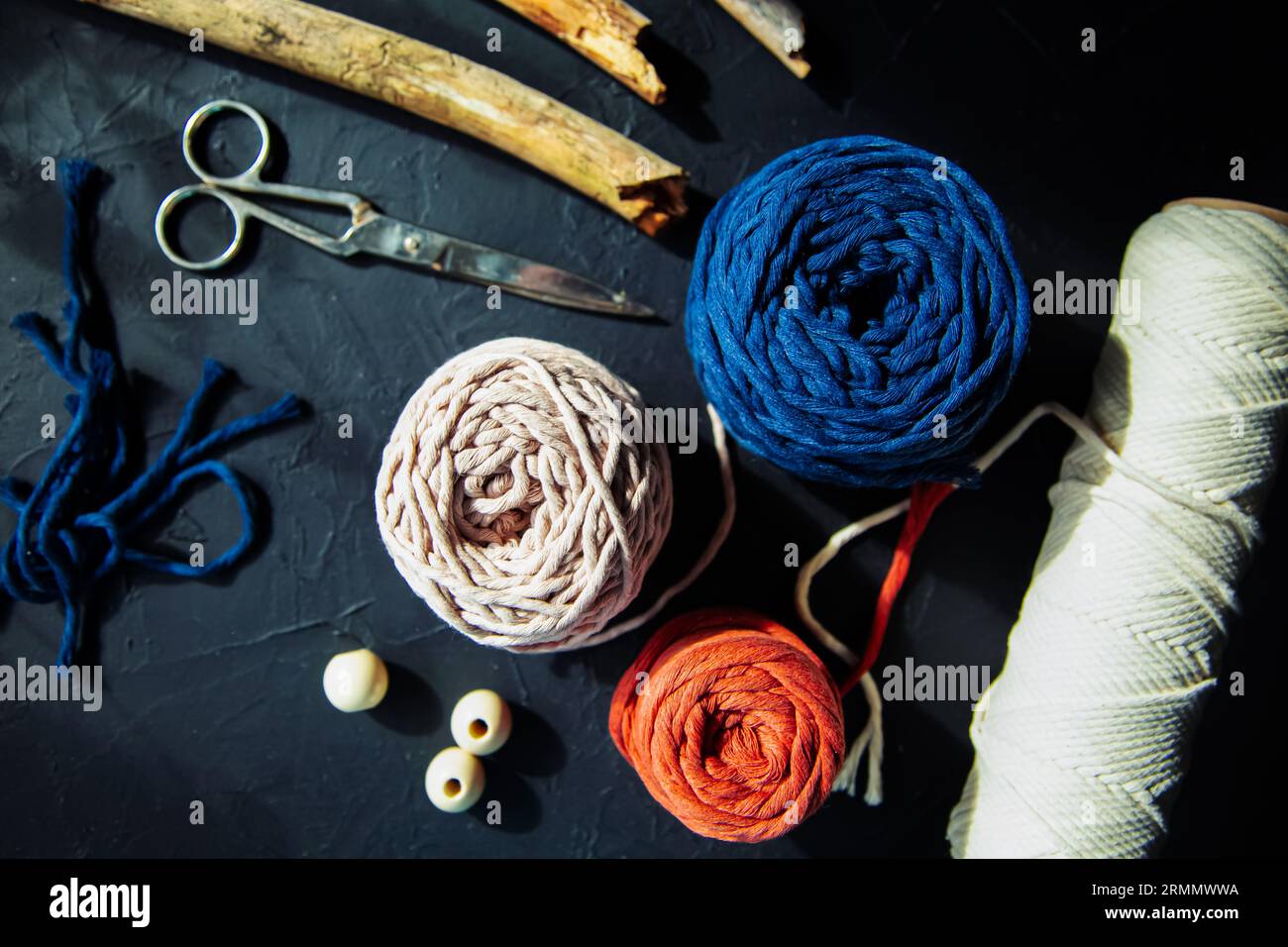 Webwerkzeuge in der Makramee-Technik. Baumwollschnüre, Schere, Treibholz, Perlen. Der Trend moderner Wohnkultur, handgefertigter, schwarzer Hintergrund. Stockfoto