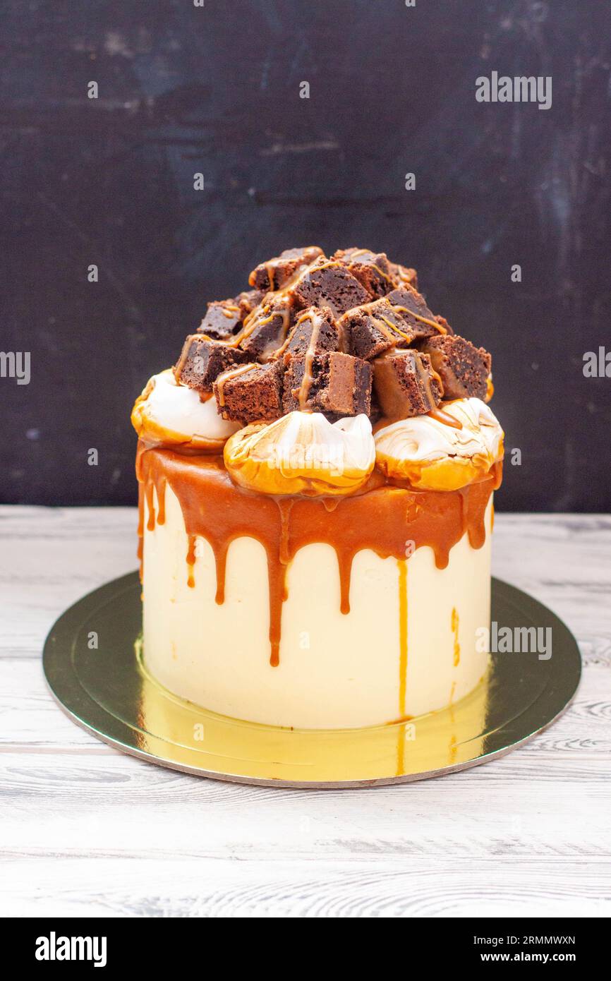 Köstlicher Vanillekuchen mit geschnittenen Brownie-Stücken, Meringue-Wolken und geschmolzener gesalzener Karamellsauce Stockfoto