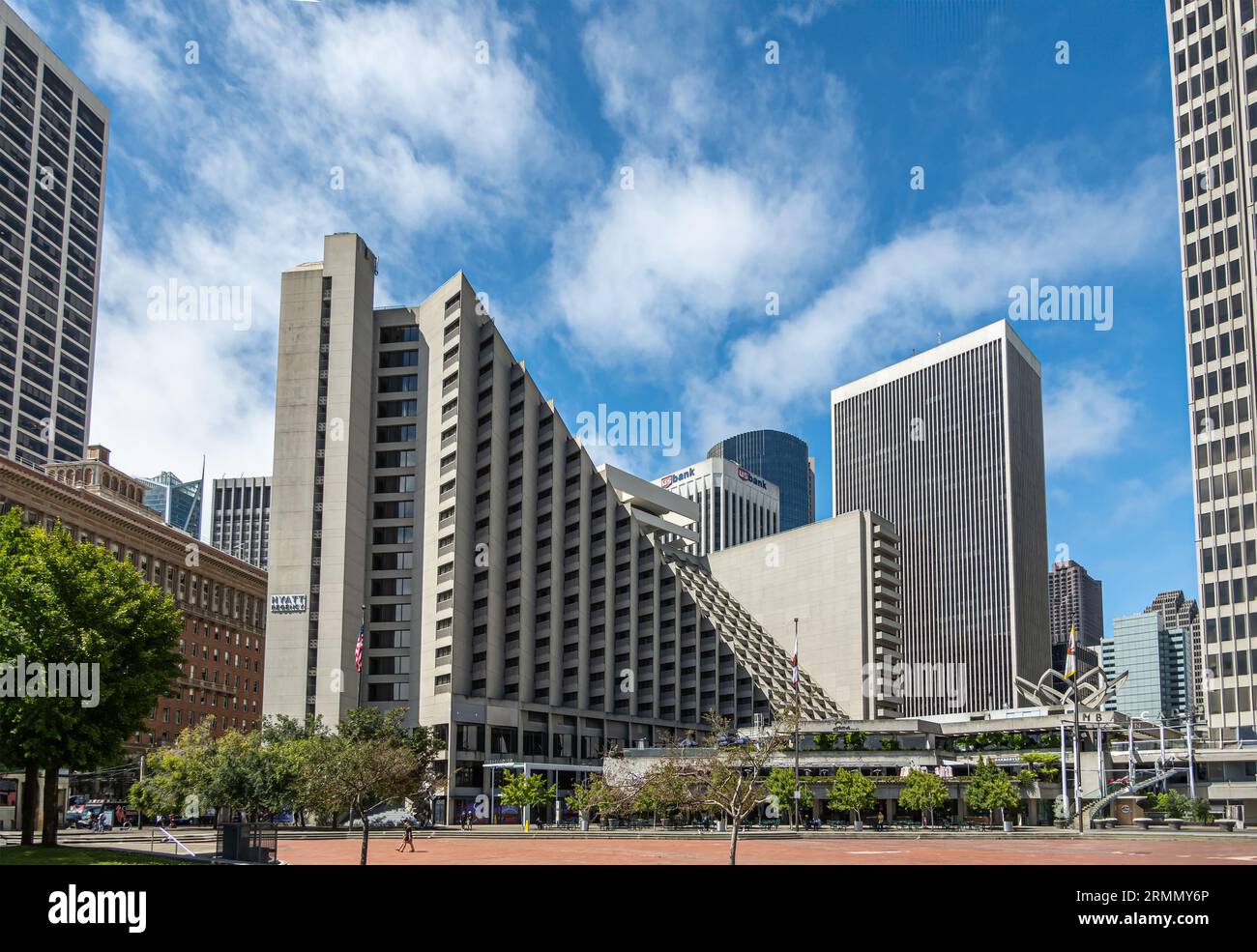 San Francisco, CA, USA - 12. Juli 2023: Das Finanzviertel ragt hinter dem Hyatt Regency Hotel auf dem Embarcadero Plaza unter blauem Wolkenbild hoch. Grünes Laub Stockfoto