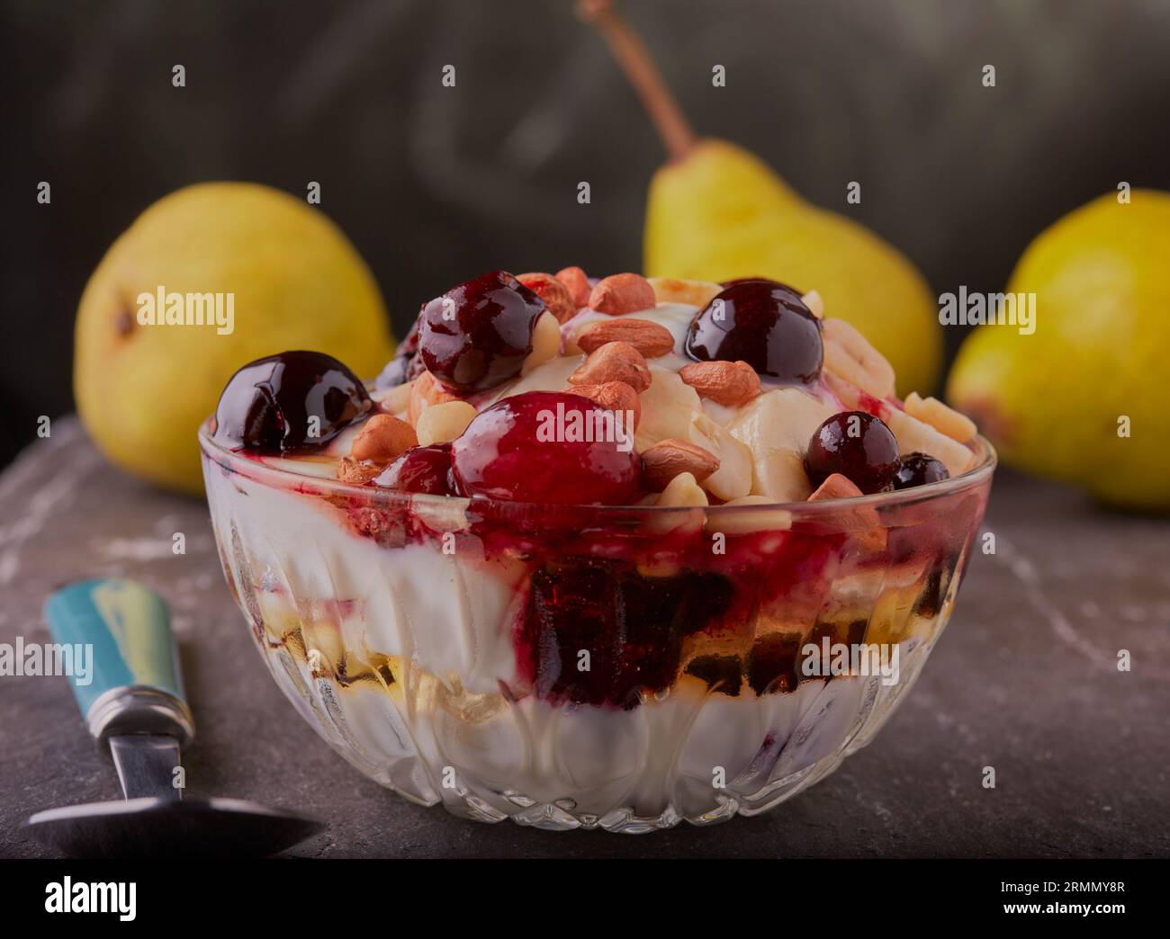 Schüssel mit gemischten Früchten, griechischem Joghurt und Honig, garniert mit Nüssen in einer Glasschale. Stockfoto