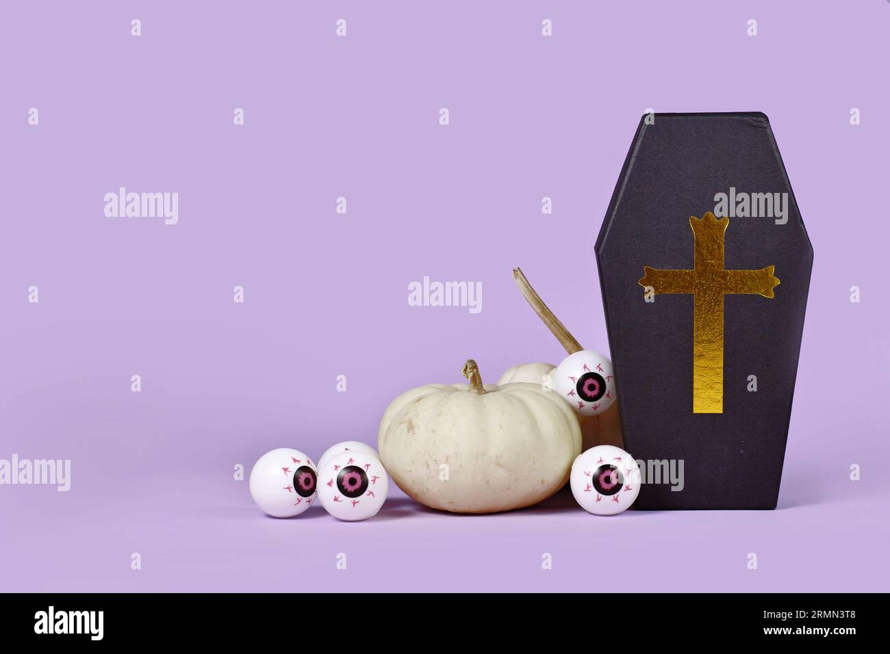 Halloween-Arrangement mit Sarg-Geschenkbox, Baby-Bambus-Kürbissen und Augäpfeln auf lila Hintergrund mit Kopierraum Stockfoto