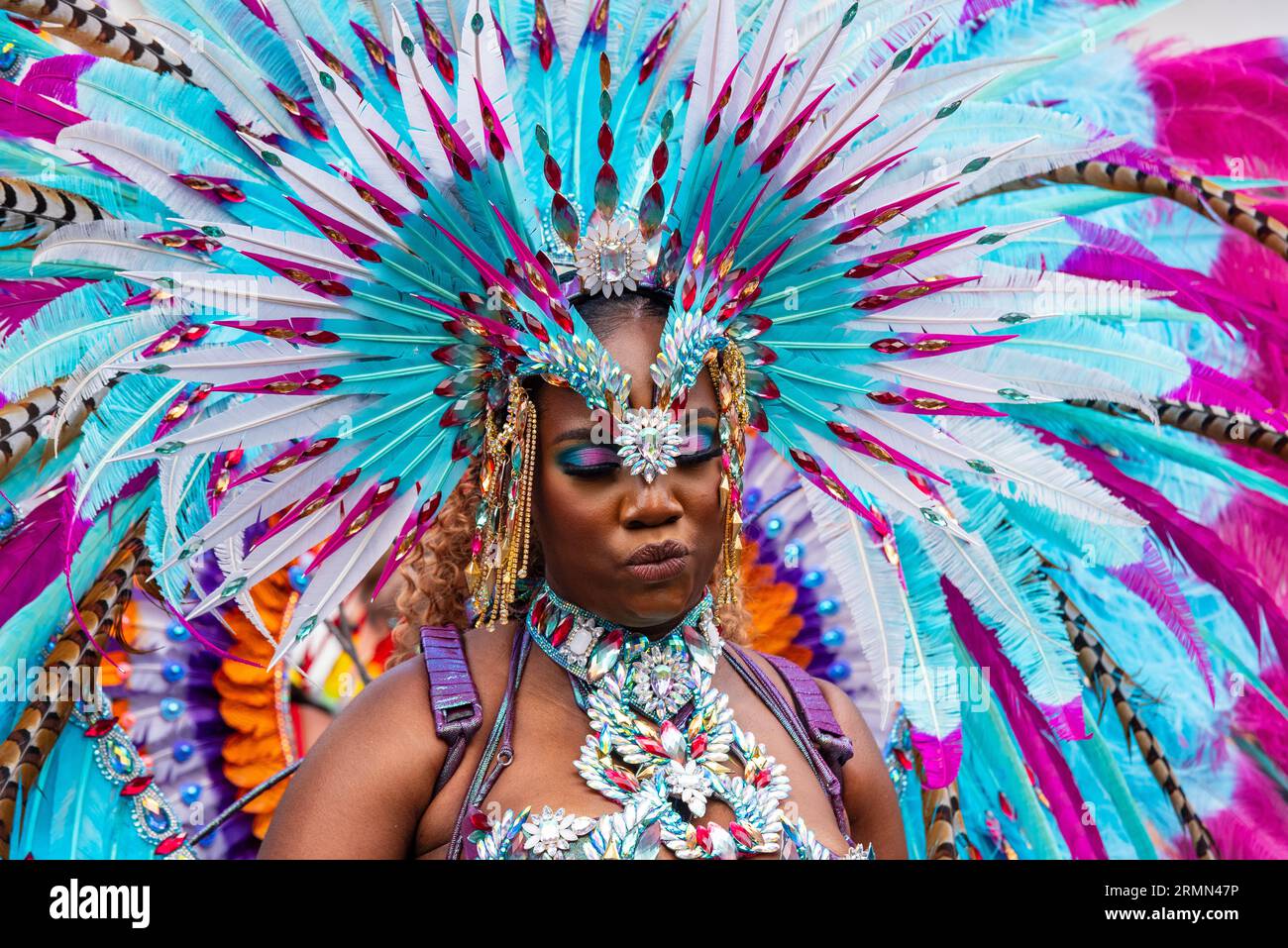 Teilnehmerin bei der Notting Hill Carnival Grand Parade 2023 in London. Aufwendiger, farbiger Gefieder-Kopfschmuck mit passendem Augenschatten Stockfoto