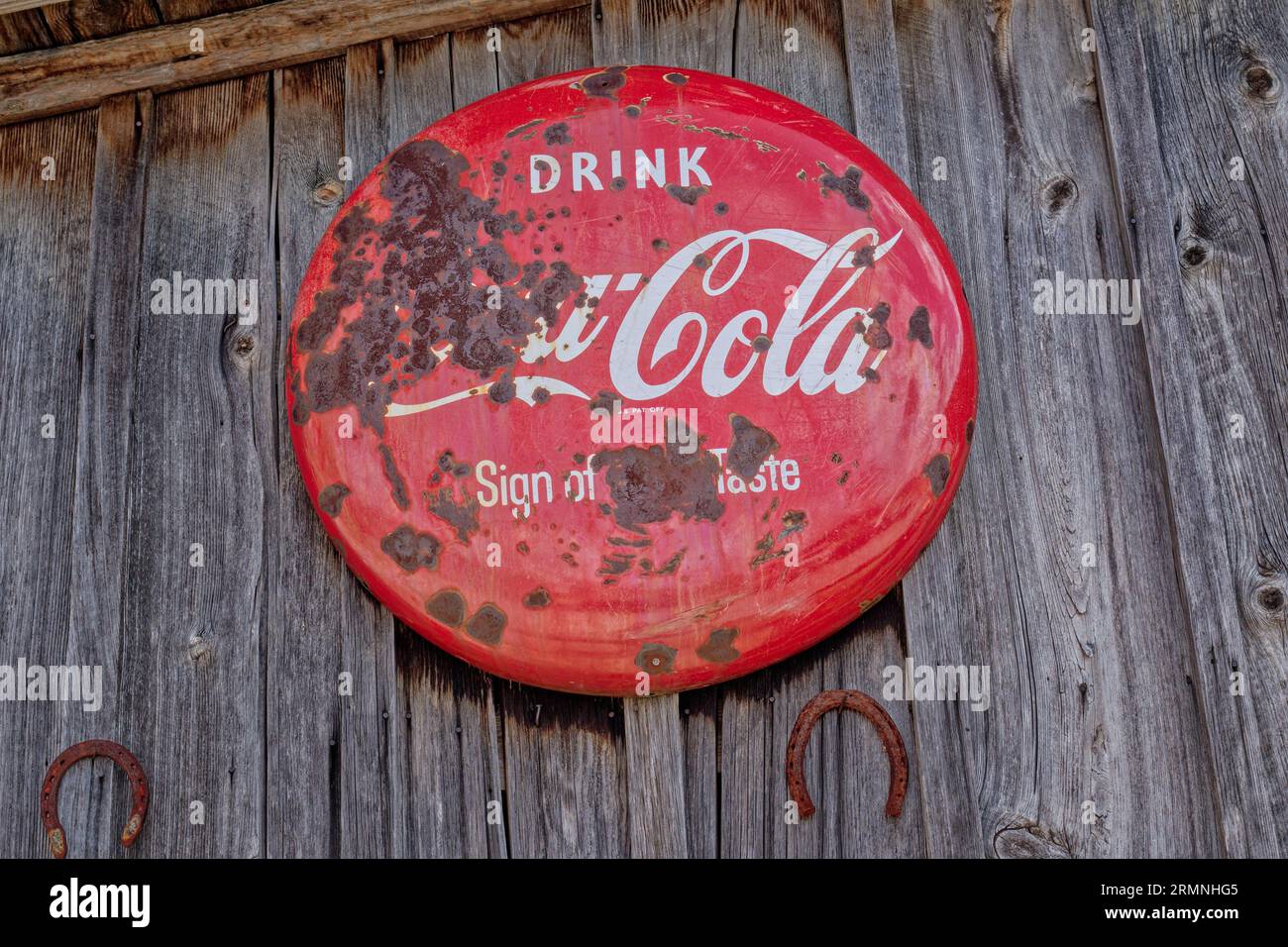 Ein altes, rundes Coca-Cola-Schild aus Porzellan im Vintage-Stil, das mit etwas Rost an einer Scheunenwand im Freien zerrüttet war Stockfoto