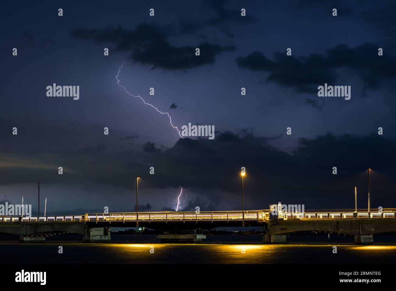 Himmel während eines schweren Sturms mit Donner und Blitz über dem Meer. Aufnahme einer Brücke mit vorbeifahrenden Autos, die eine Spur aus Licht erzeugen. Tornado kommt. Stockfoto