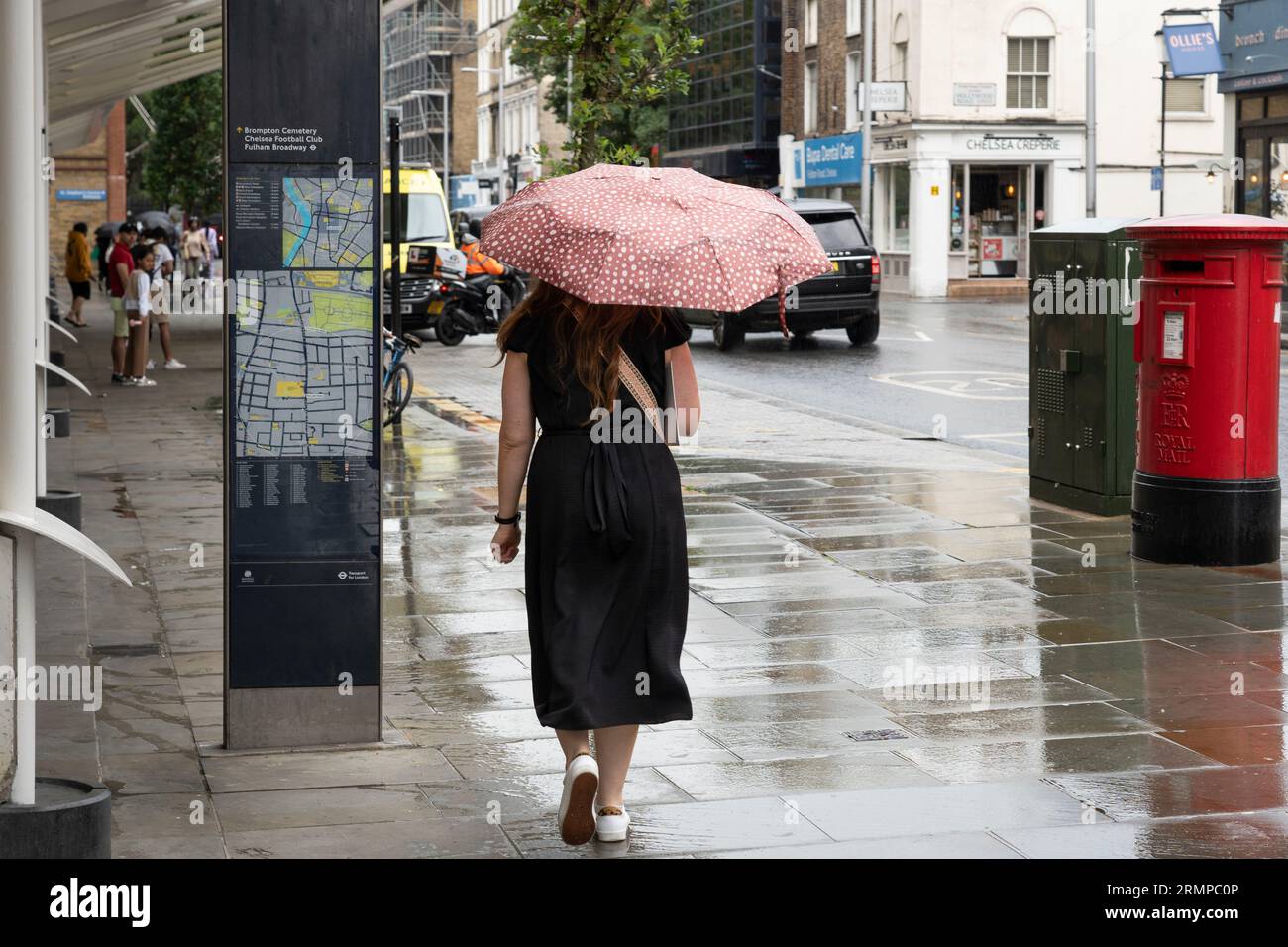 Eine Frau, die im Regen draußen spaziert und einen Regenschirm vor dem Chelsea Hospital, London, Großbritannien, hält Stockfoto