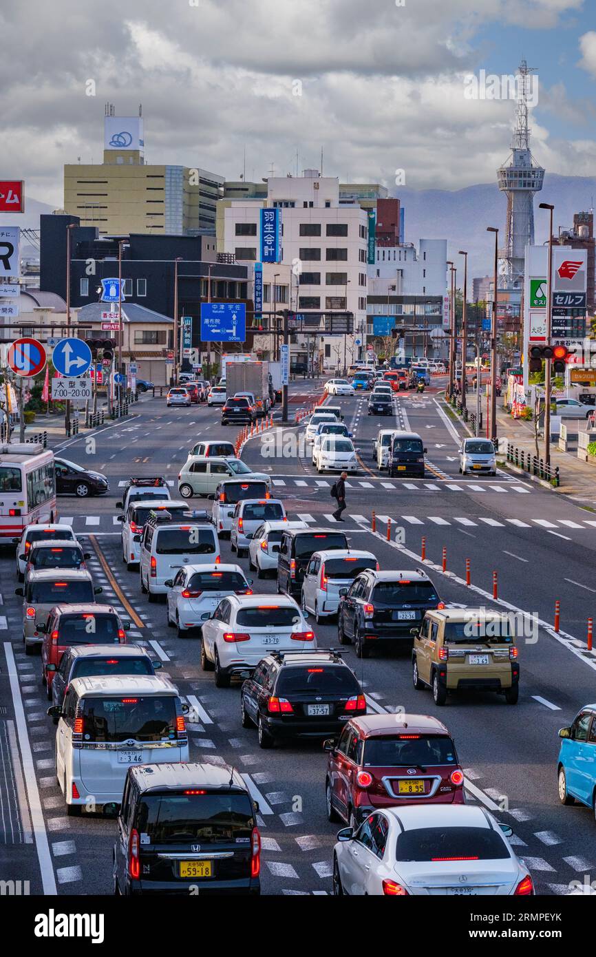 Japan, Kyushu, Beppu. Verkehr am späten Nachmittag auf der National Route 10 durch die Innenstadt von Beppu. Beppu Tower und Aussichtsplattform in der Ferne. Stockfoto