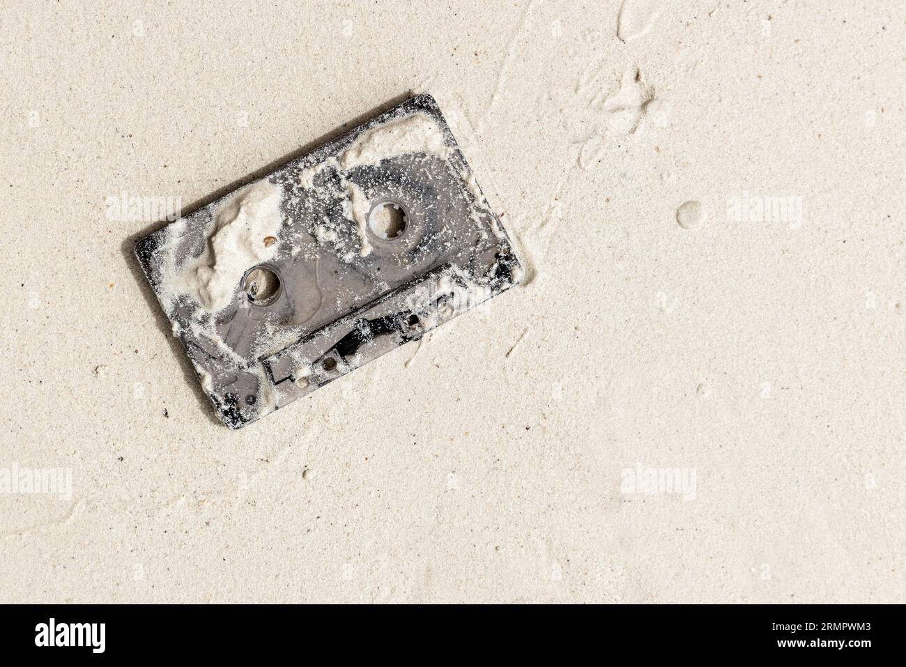 Gebrauchte Tonbandkassette liegt auf nassweißem Sand am Strand, Draufsicht Stockfoto
