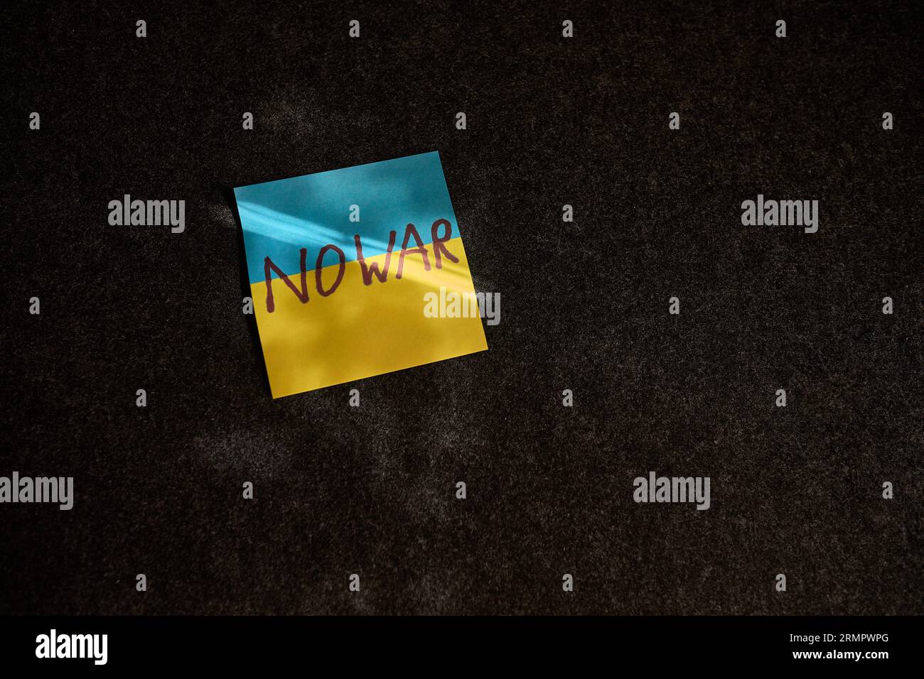 Der Aufkleber in Form der ukrainischen Flagge liegt. Auf einer dunklen Oberfläche fällt ein Sonnenstrahl darauf Stockfoto