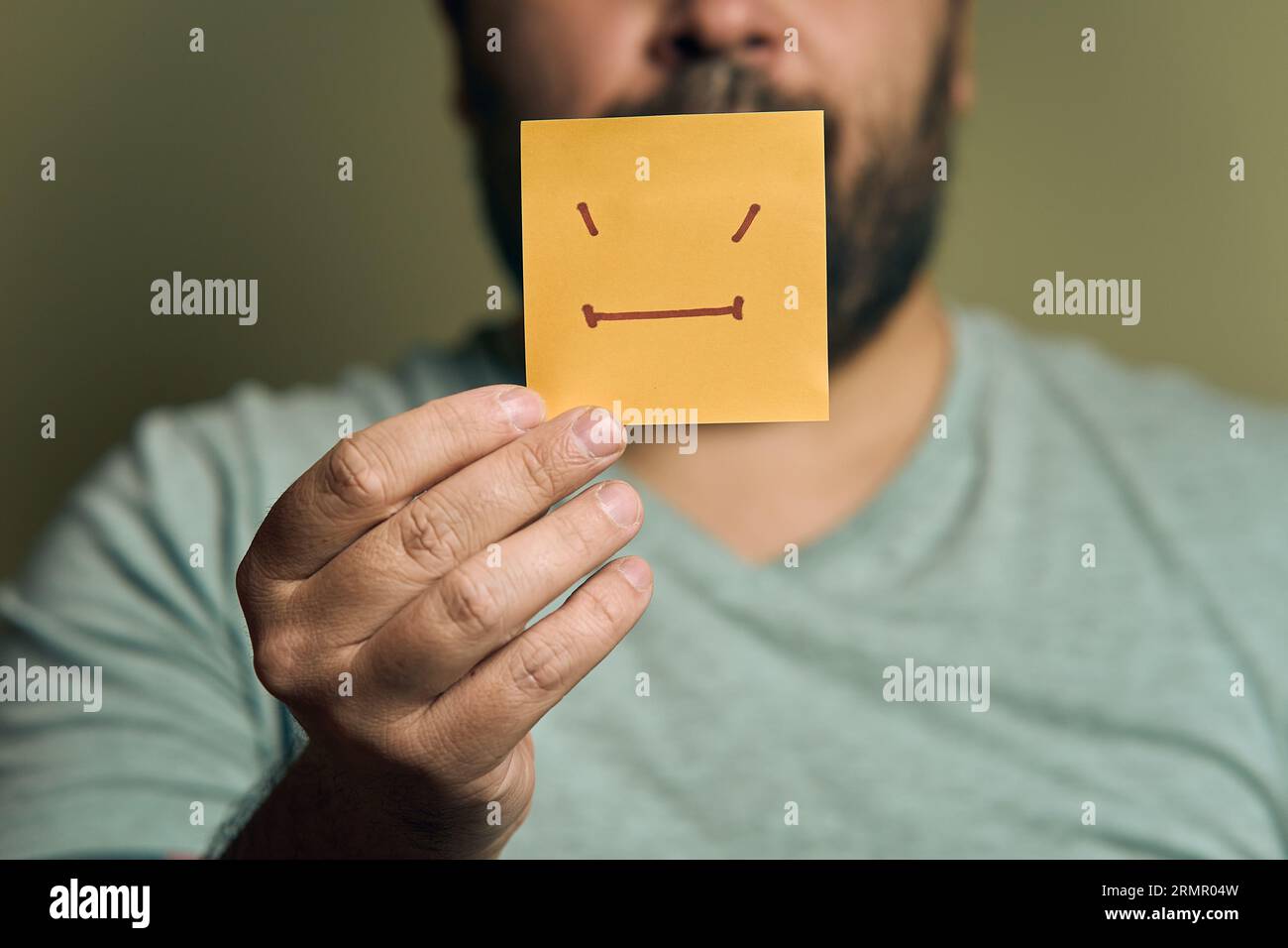 Ein bärtiger Europäer hält einen orangefarbenen Aufkleber mit einem unglücklichen Lächeln vor sich Stockfoto