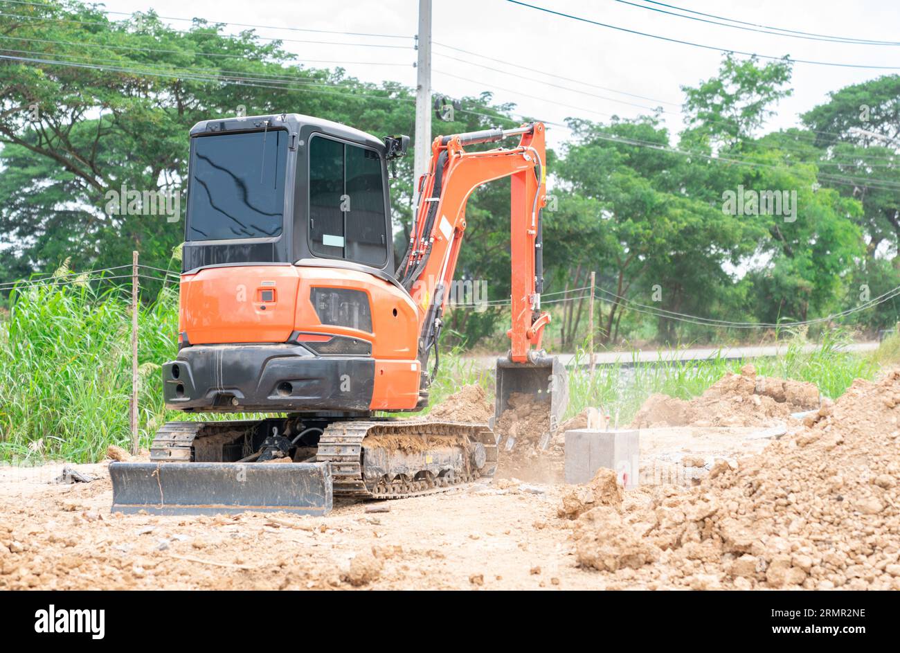 Arbeiter, der einen Minibagger benutzt, um ein Loch aus Fundamentstapel auf der Baustelle zu bedecken. Stockfoto