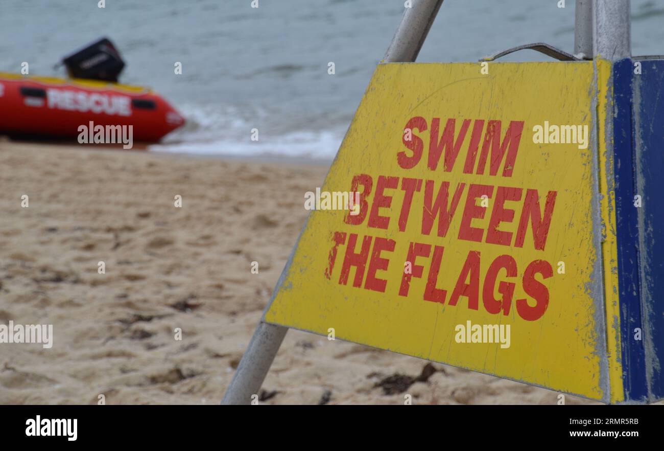 Warnschild zum Schwimmen zwischen den Flaggen an einem Strand in Queensland mit rauem Meer und einem Rettungsboot im Hintergrund Stockfoto