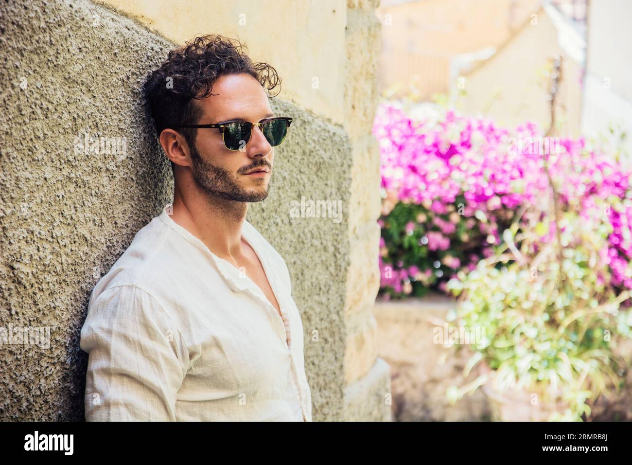 Ein Mann, der eine Sonnenbrille trägt und sich an eine Wand lehnt Stockfoto