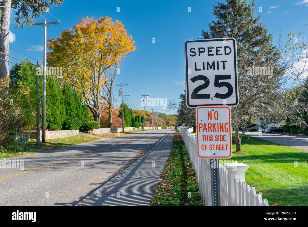 Traditionelles amerikanisches Geschwindigkeitslimit und keine Parkschilder über einem weißen Zaun an der Ocean Ave, Kennebunkport, Maine, USA, gesäumt von goldenen Fallbäumen. Stockfoto
