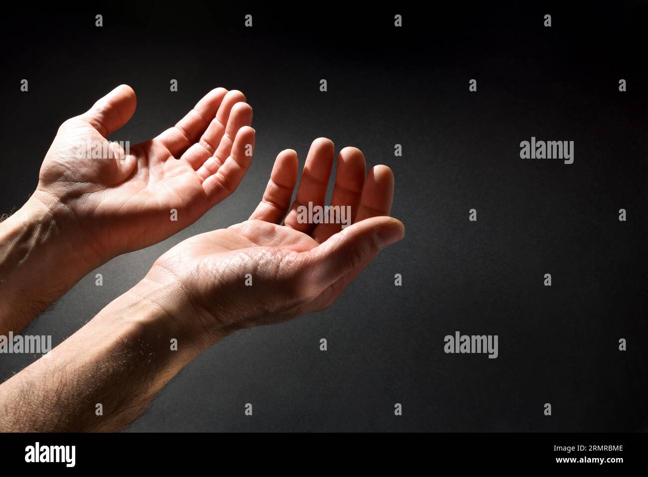 Betender Mann mit erhobenen Händen im Kontrast zum Lichtstrahl auf dunklem, isoliertem Hintergrund. Von oben erhöhter Blick. Stockfoto